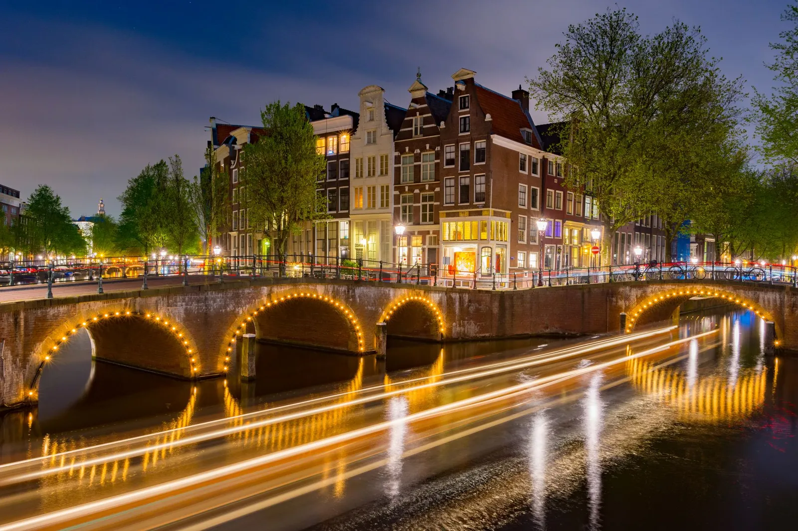 Captivating long exposure of illuminated Amsterdam canal and historic buildings at night.