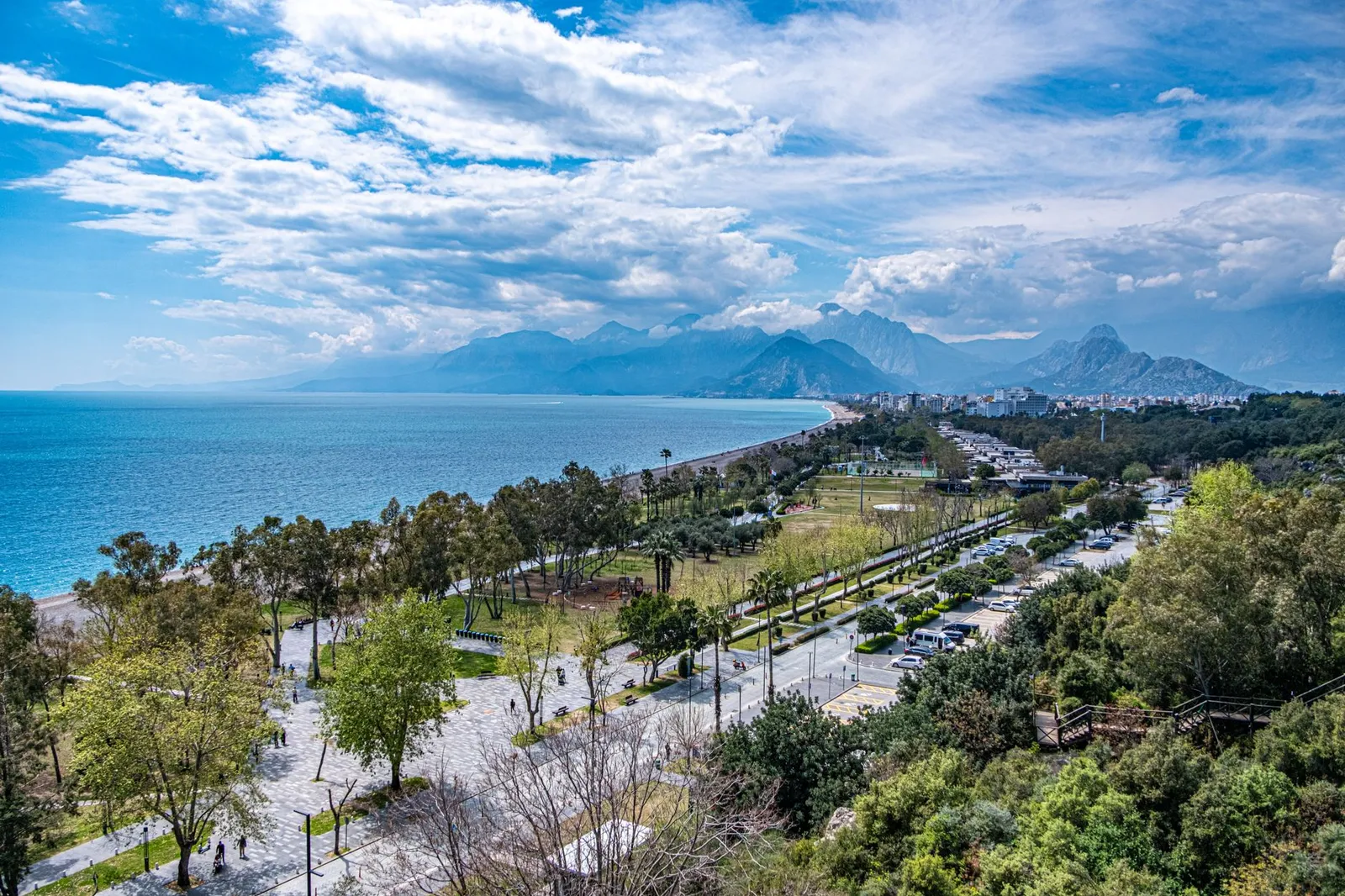 A breathtaking view of Antalya's coastline with lush greenery and distant mountains under a vibrant sky.