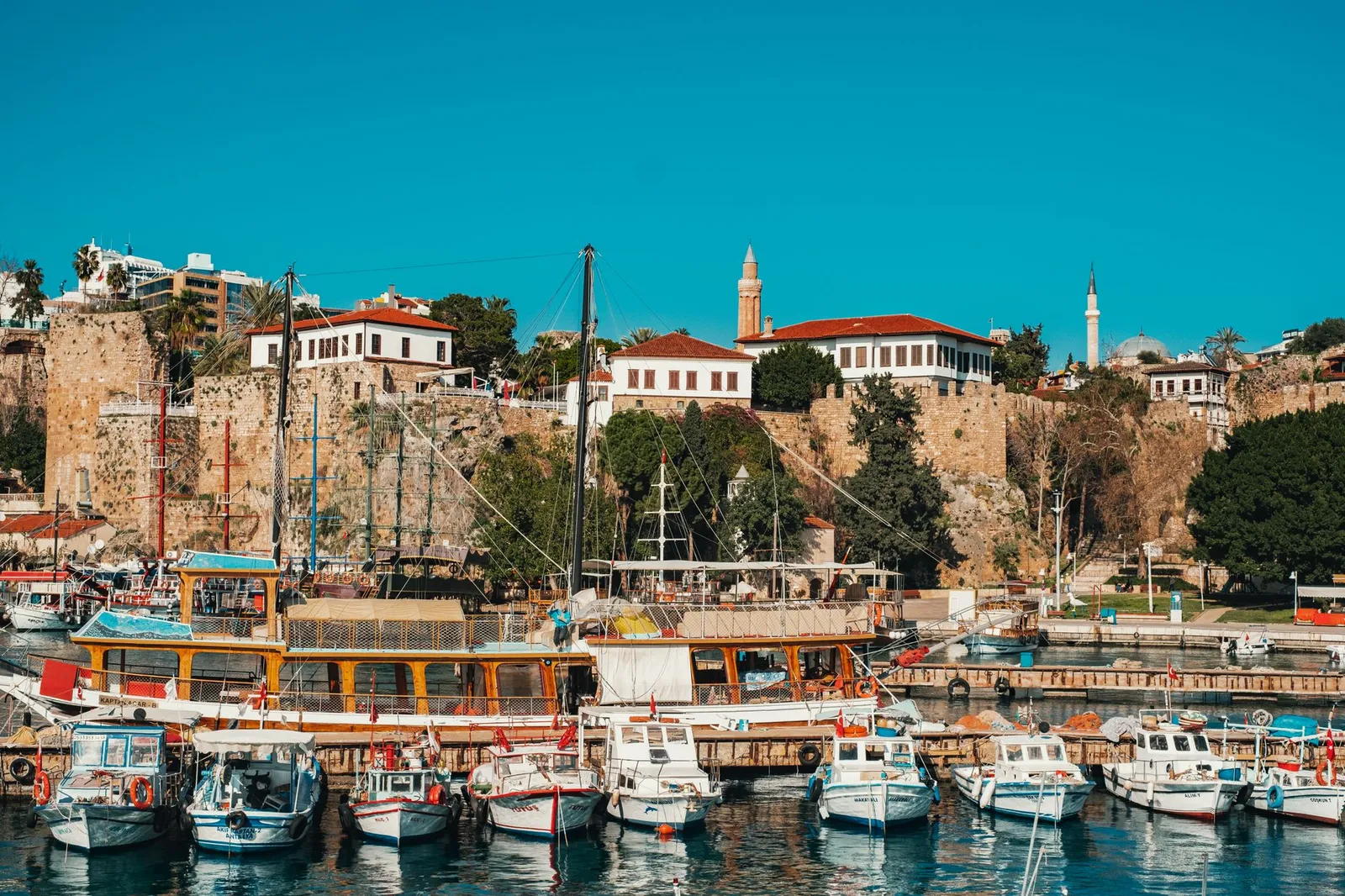 Charming harbor scene with docked boats and ancient fort in Antalya, Türkiye.