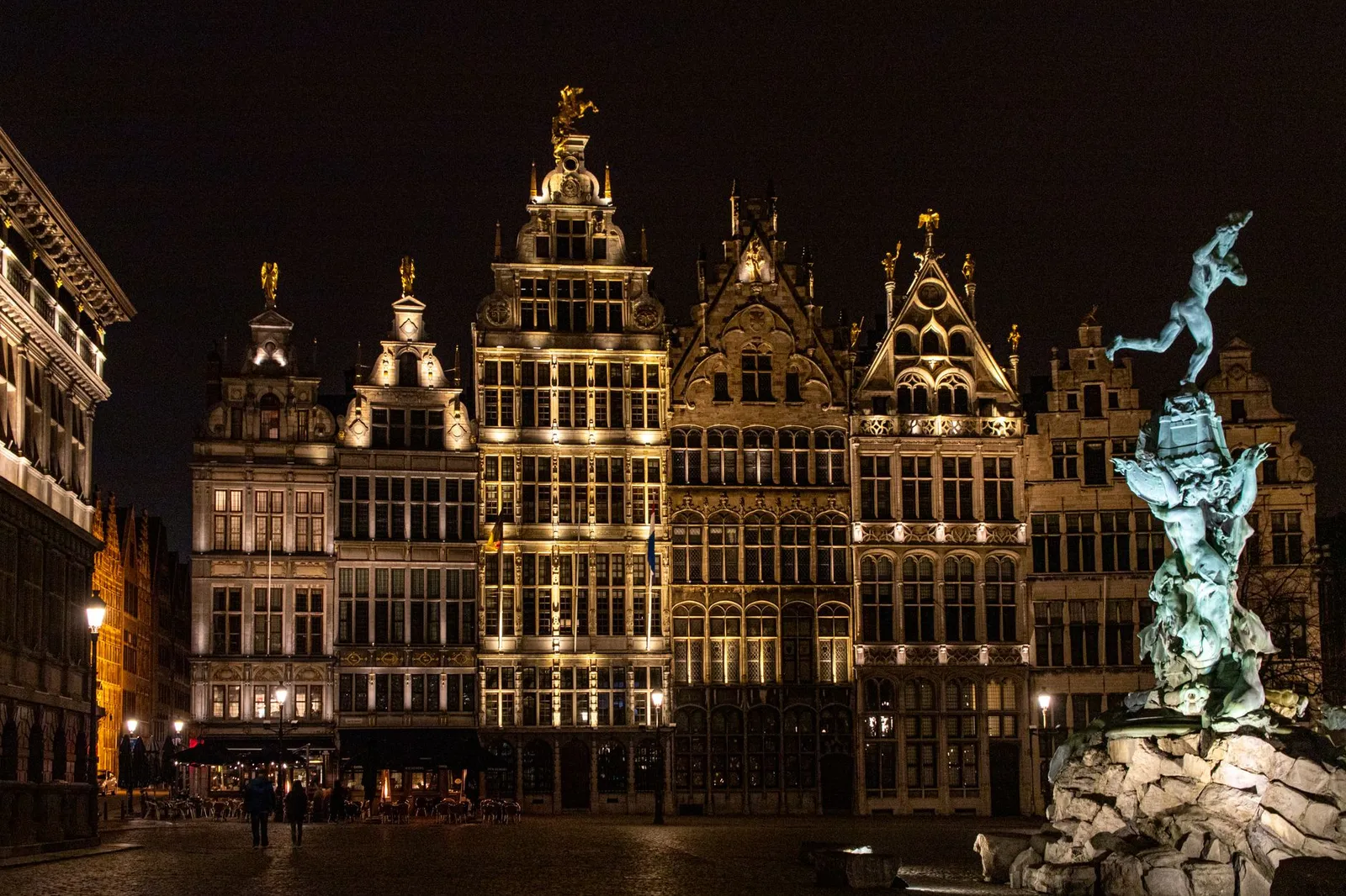Illuminated historic buildings and Brabo Fountain at Antwerp Market Square, captured at night.