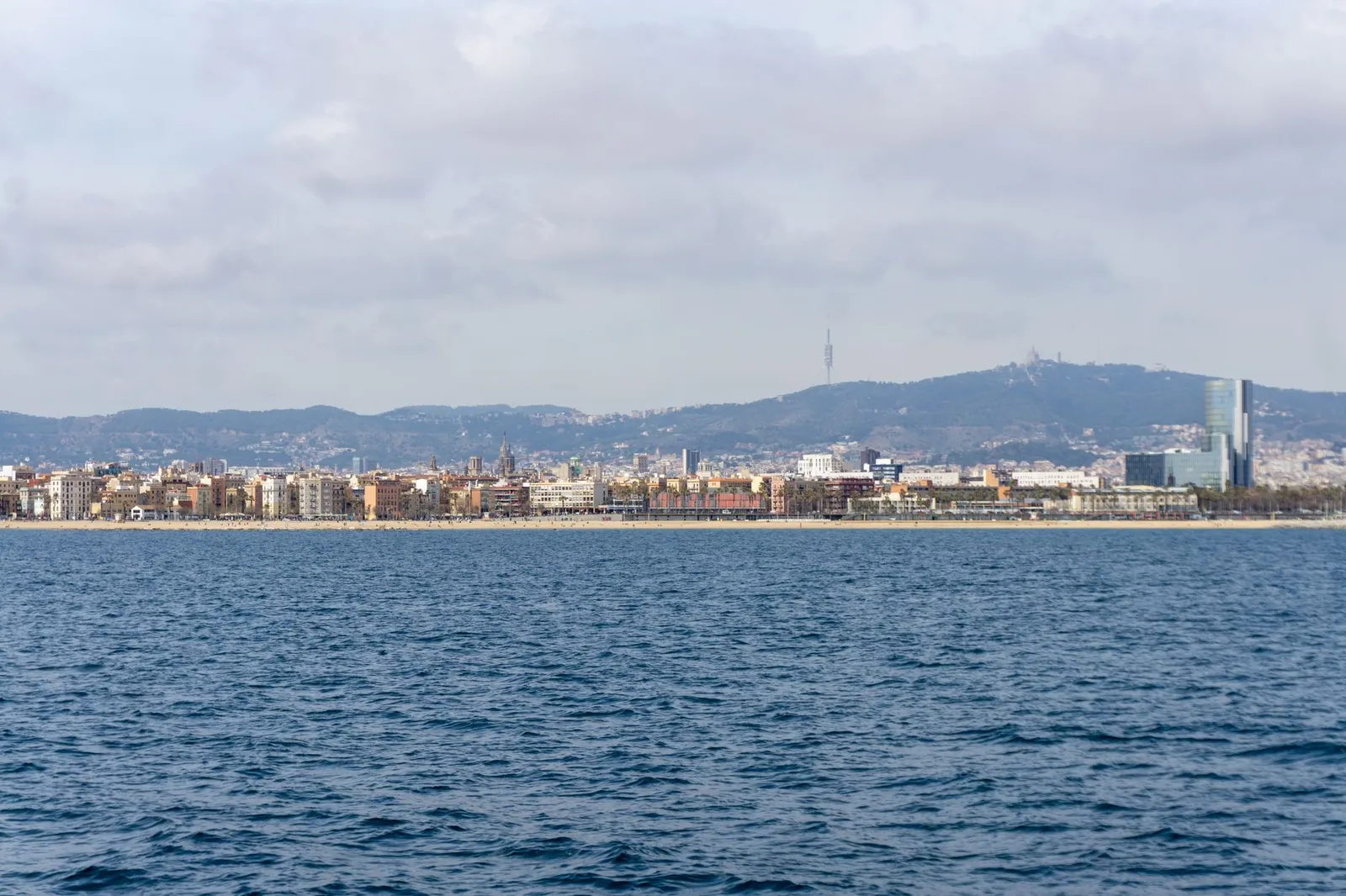 Stunning panoramic view of Barcelona coastline with urban skyline and distant hills under a cloudy sky.