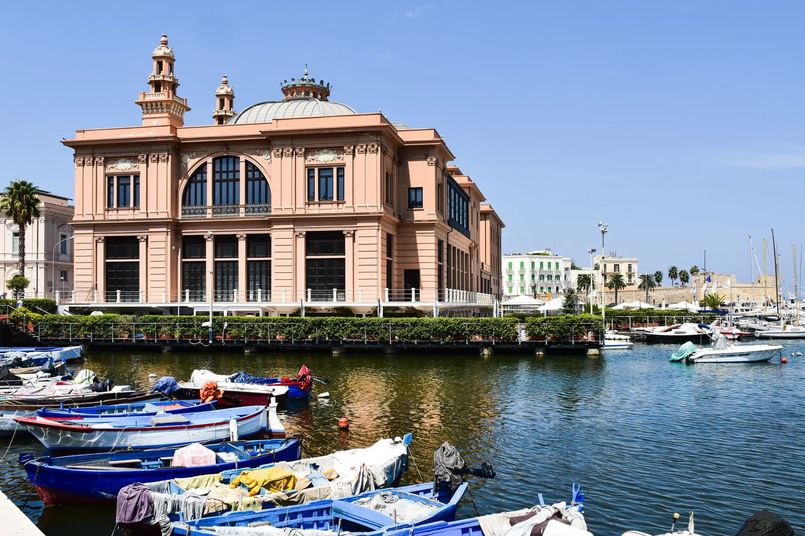 Historic pink theater overlooking the waterfront with colorful boats in Bari, Apulia, Italy.