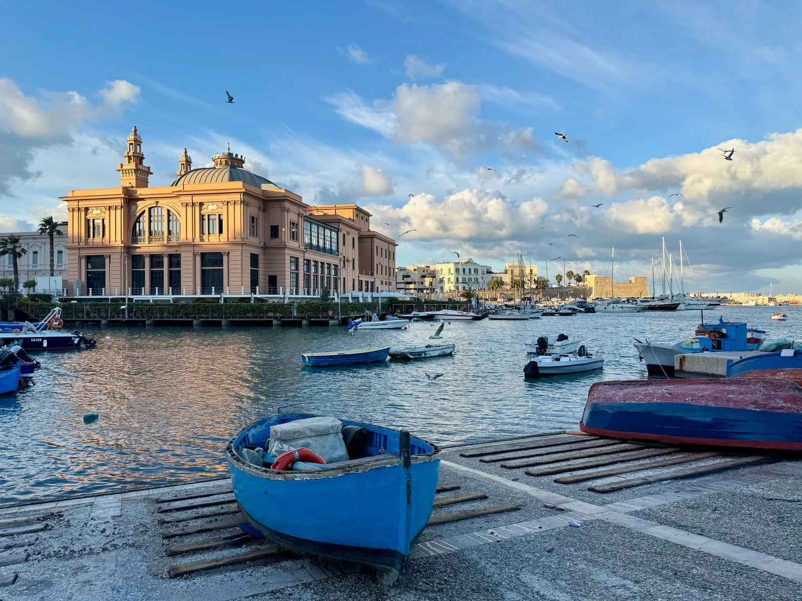 Charming harbor scene in Bari, Italy with boats, seagulls, and a historic building under a blue sky.