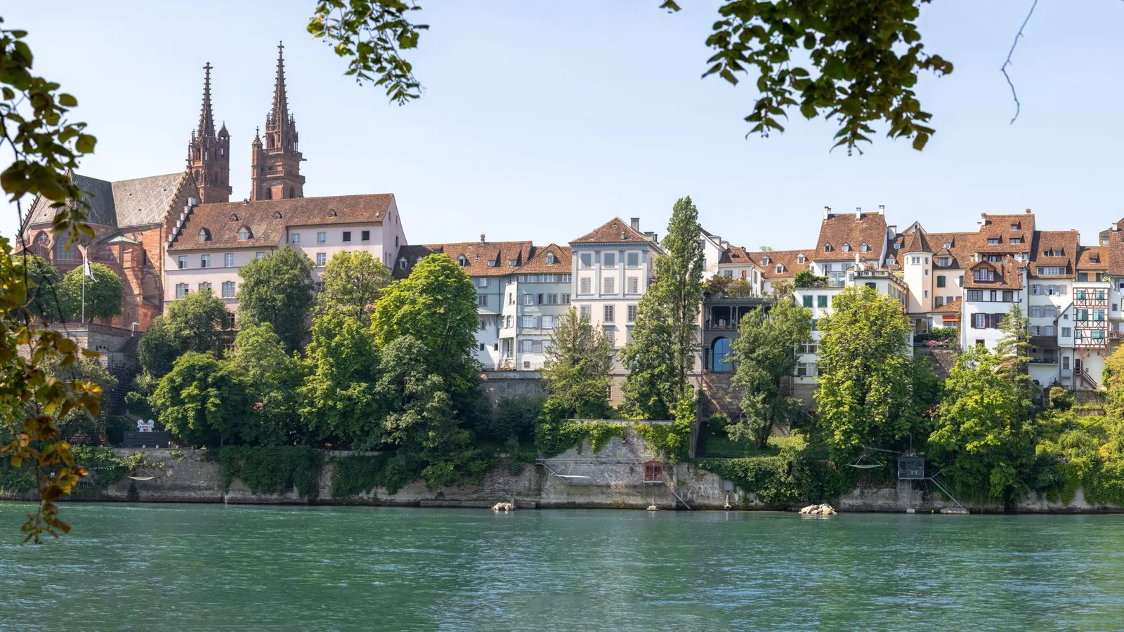 Charming view of Basel's historic buildings and lush greenery along the scenic Rhine River.