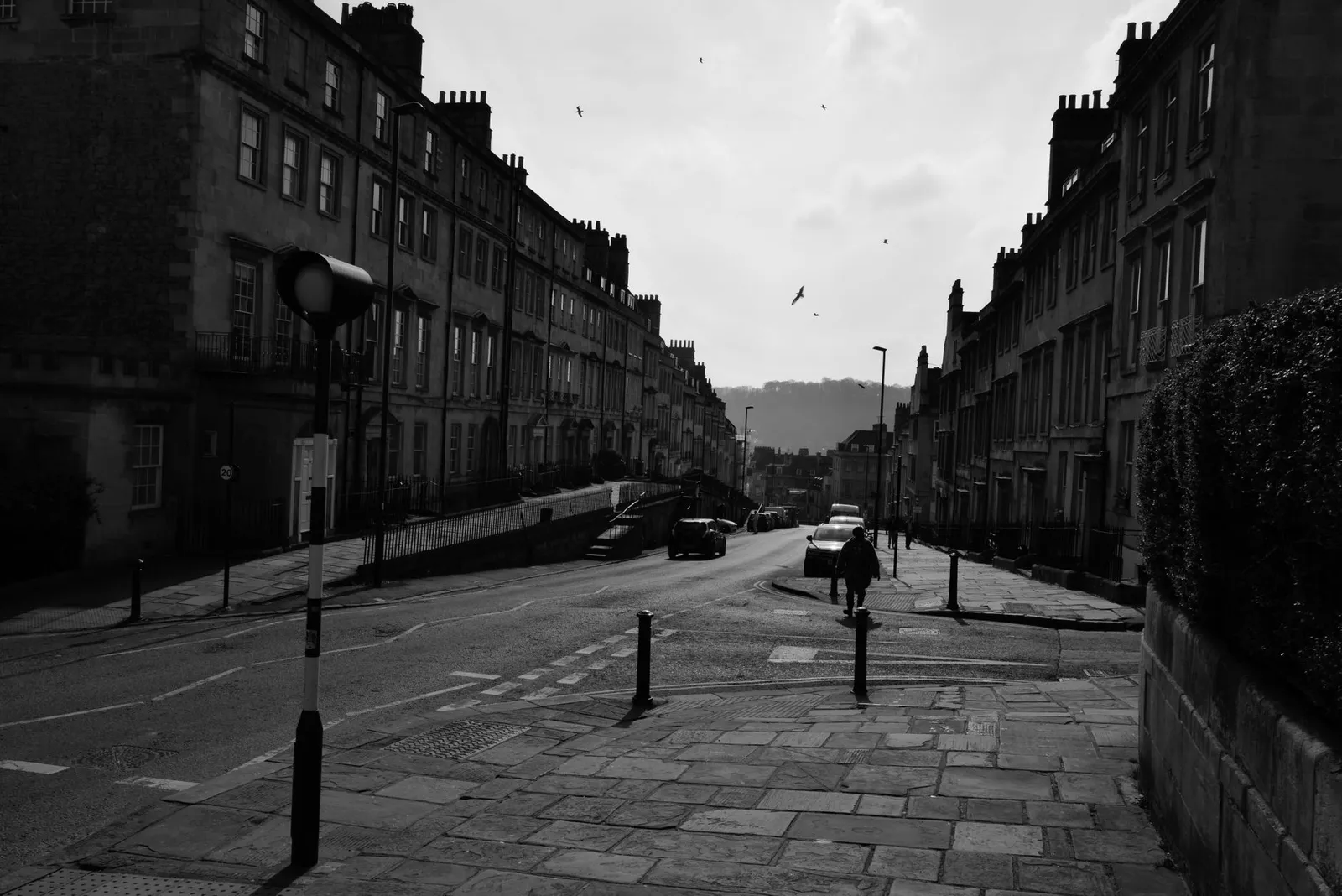 Monochrome image of a historic street in Bath, England, featuring classic architecture and urban scenery.