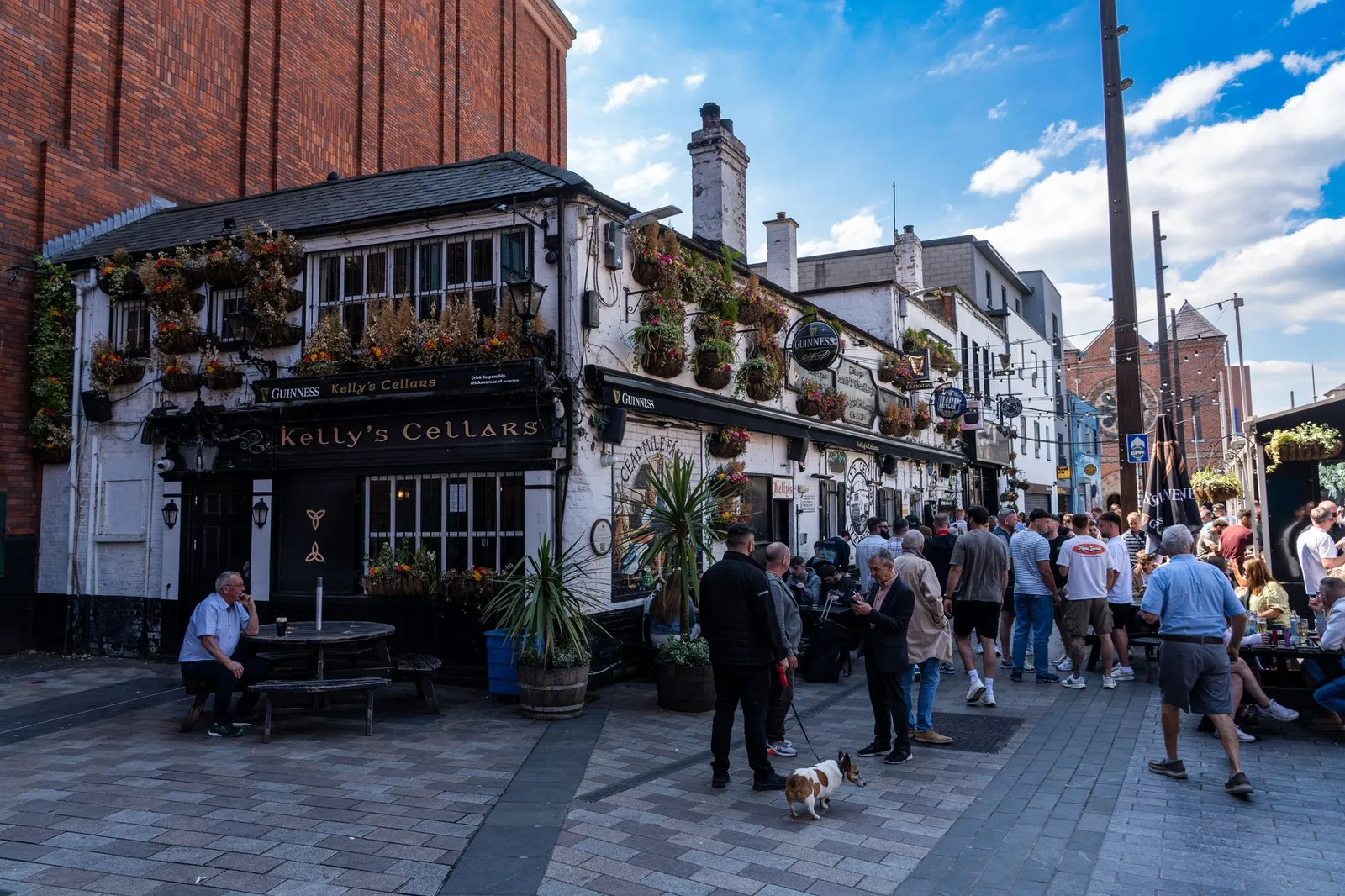 Crowds gather outside Kelly's Cellars in Belfast, enjoying a sunny day in Ireland's historic pub scene.
