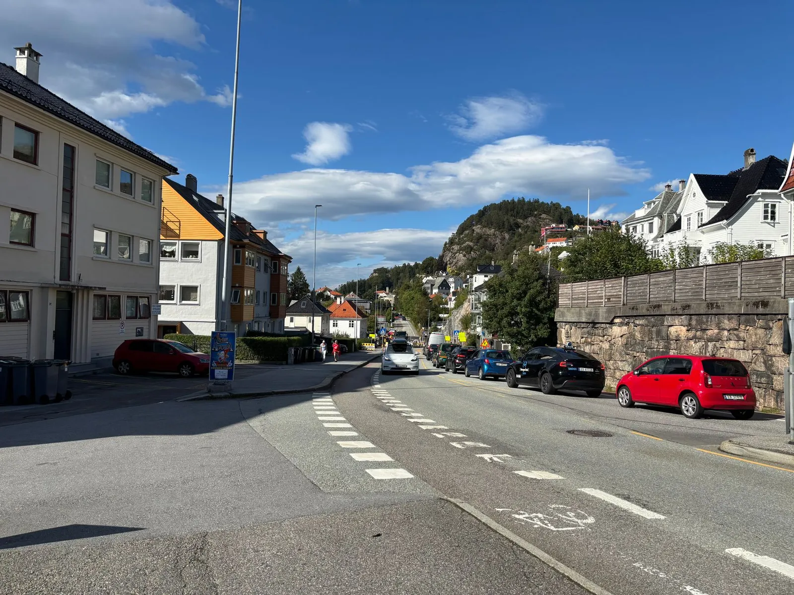 Vibrant daytime street scene in Bergen, Norway, with city architecture and scenic hill view.