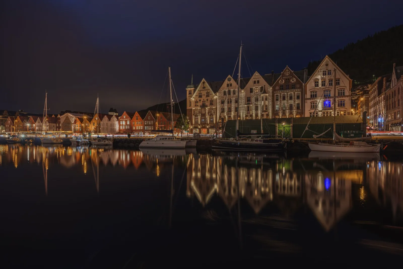View of the illuminated Bryggen Wharf in Bergen, Norway at night, reflecting in the calm water.