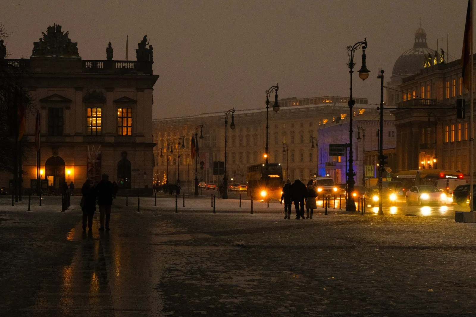 A winter evening street scene in Berlin with illuminated buildings and pedestrians.