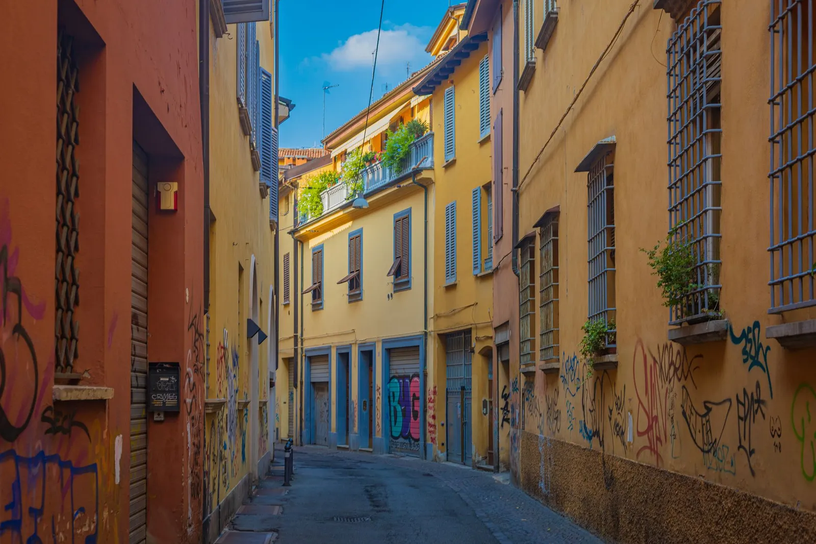 Discover a vibrant alley in Bologna with colorful graffiti and classic Italian architecture.