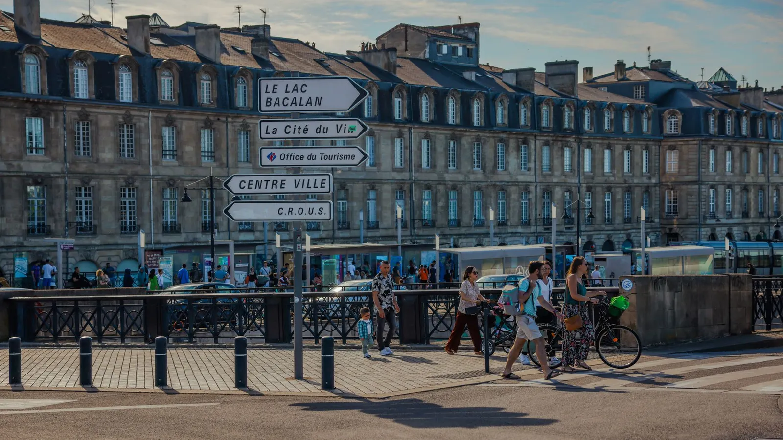 People walking near directional signs in Bordeaux, featuring historic architecture and bustling streets.