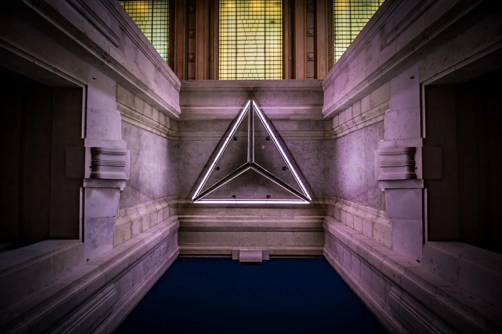 Low-angle view of a neon triangle in ornate Milan architecture, creating a modern and classic blend.