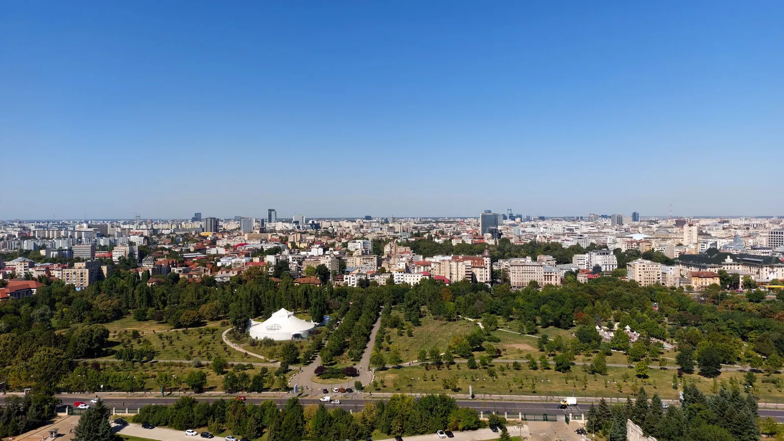 Aerial view of Bucharest cityscape with green parks and skyline under clear blue sky.