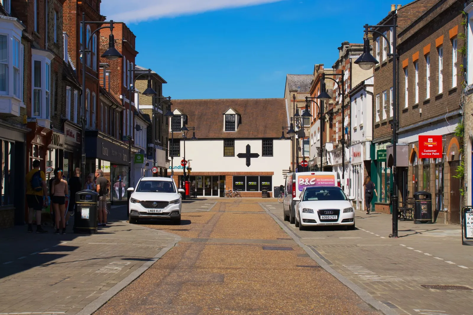 Sunny day on a lively street in Cambridge, England showcasing shops and parked cars.