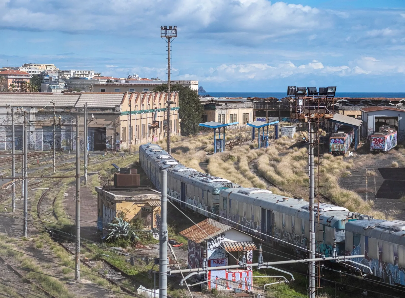 A vast abandoned train yard with graffiti-covered cars and buildings in Catania, Sicily.