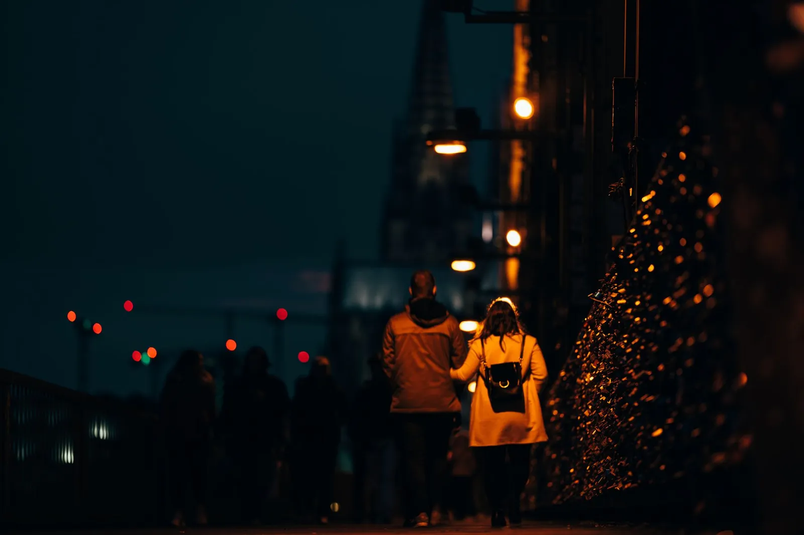 Couple walking on an illuminated street in Cologne at night, with the cathedral in view.