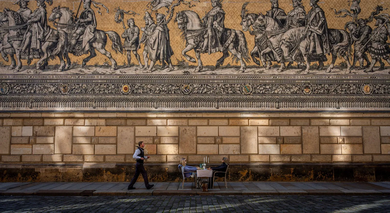 Historic mosaic wall with people enjoying a meal in Dresden.