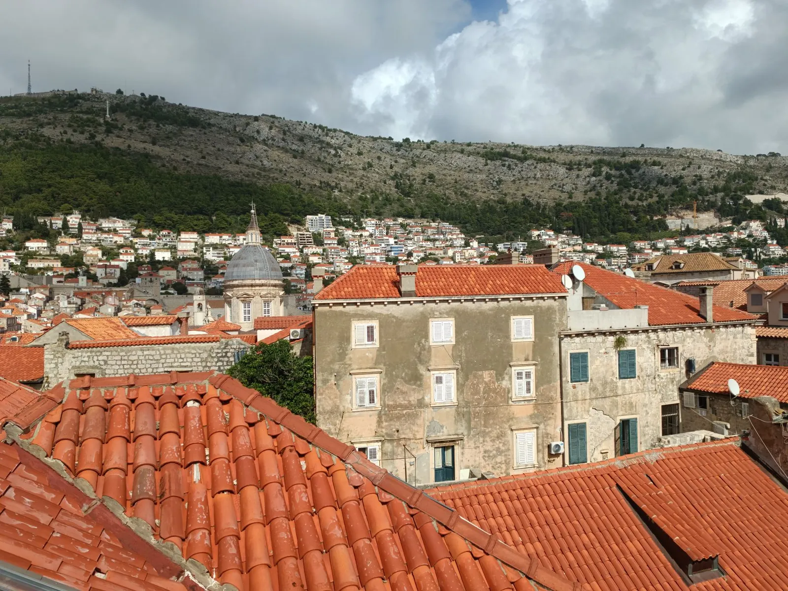 Explore the picturesque rooftop view of Dubrovnik's historic Old Town framed by lush green hills.