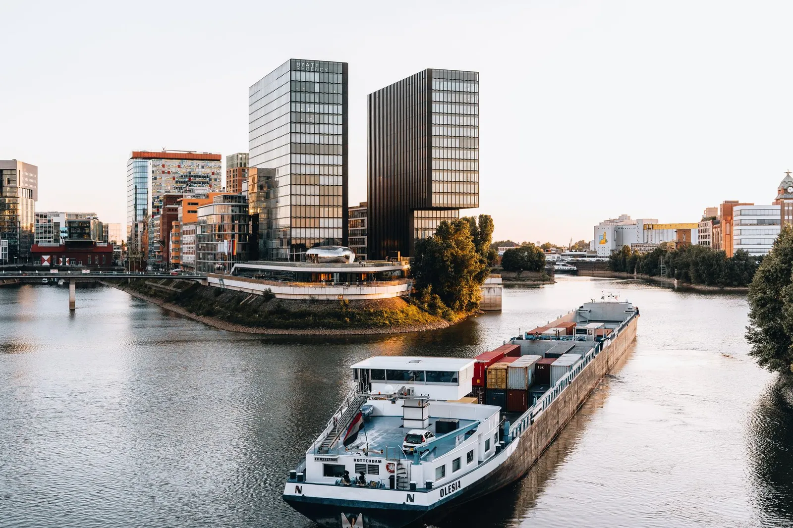 A modern barge sailing through Düsseldorf's urban river surrounded by contemporary architecture at sunset.