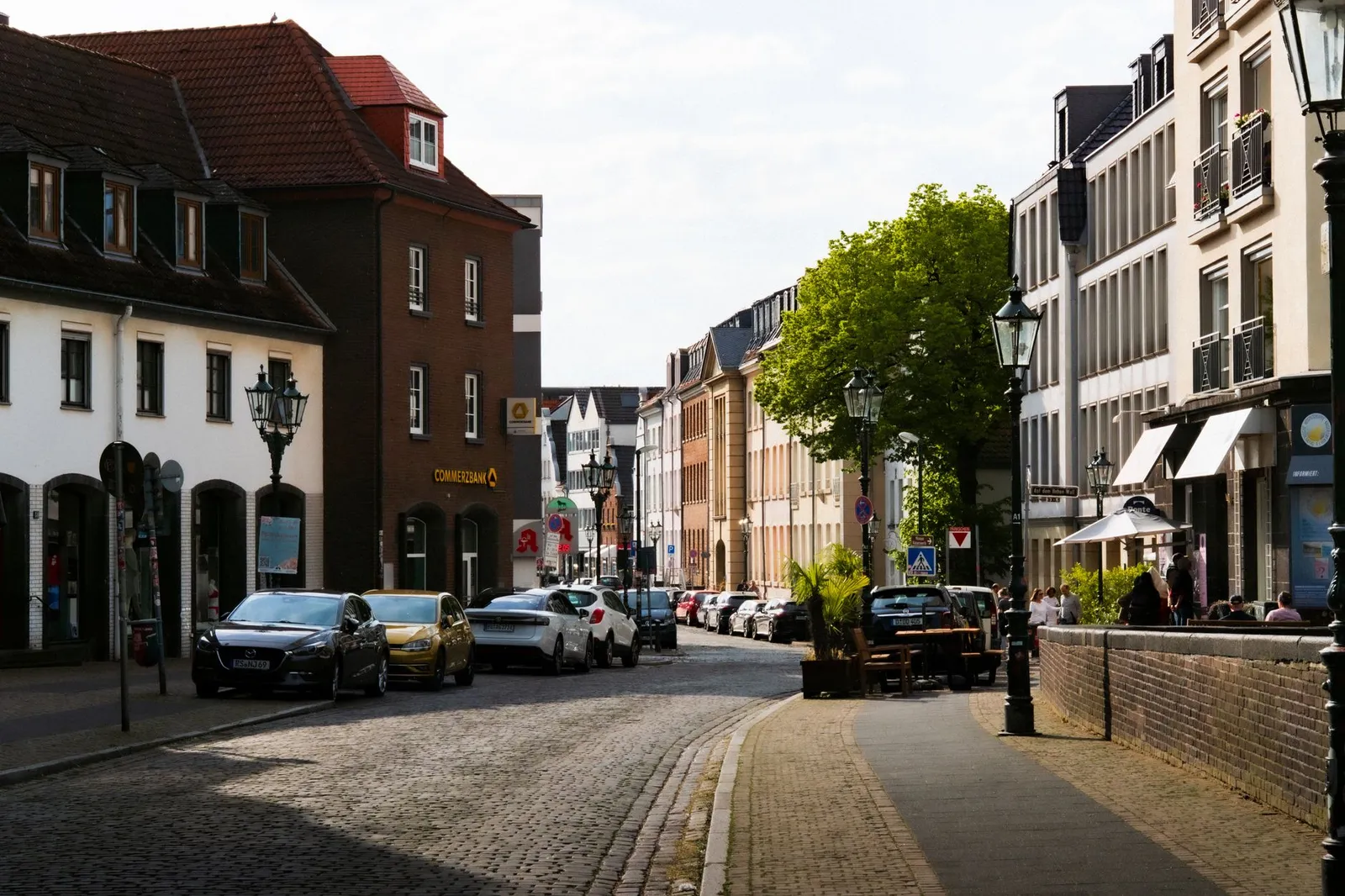 Sunny day on a cobblestone street in Düsseldorf, Germany with parked cars and classic architecture.