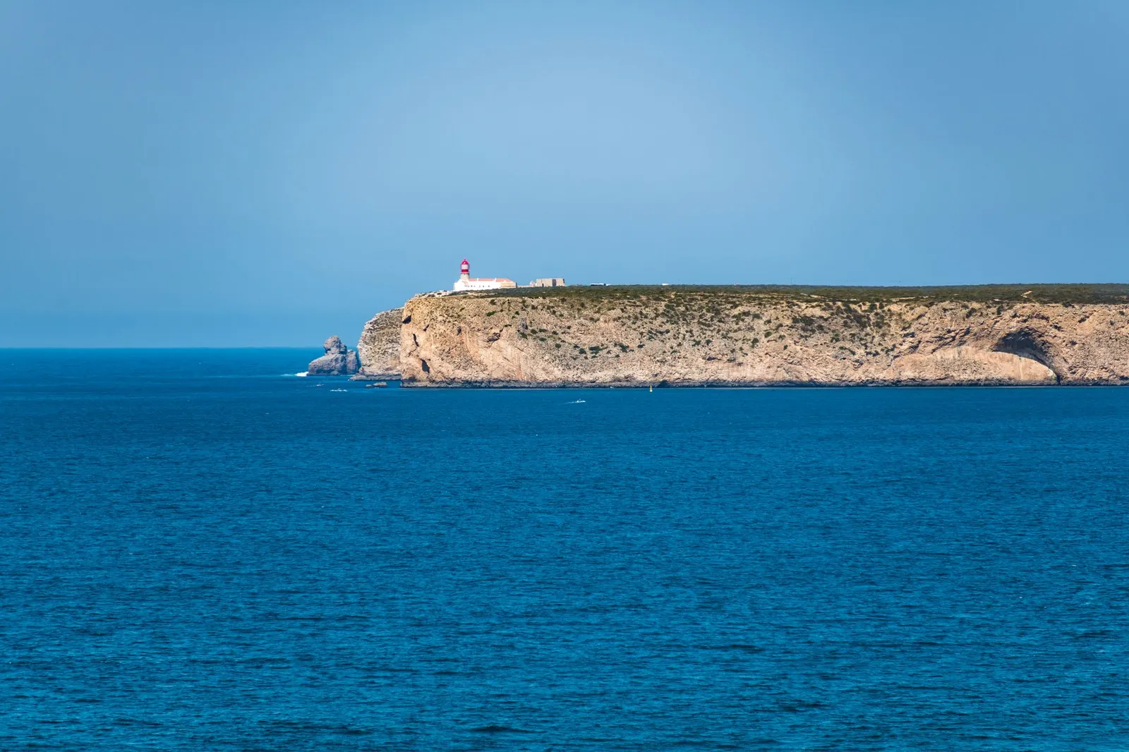 Scenic view of the Sagres lighthouse perched on cliffs above the blue Atlantic Ocean in Faro, Portugal.