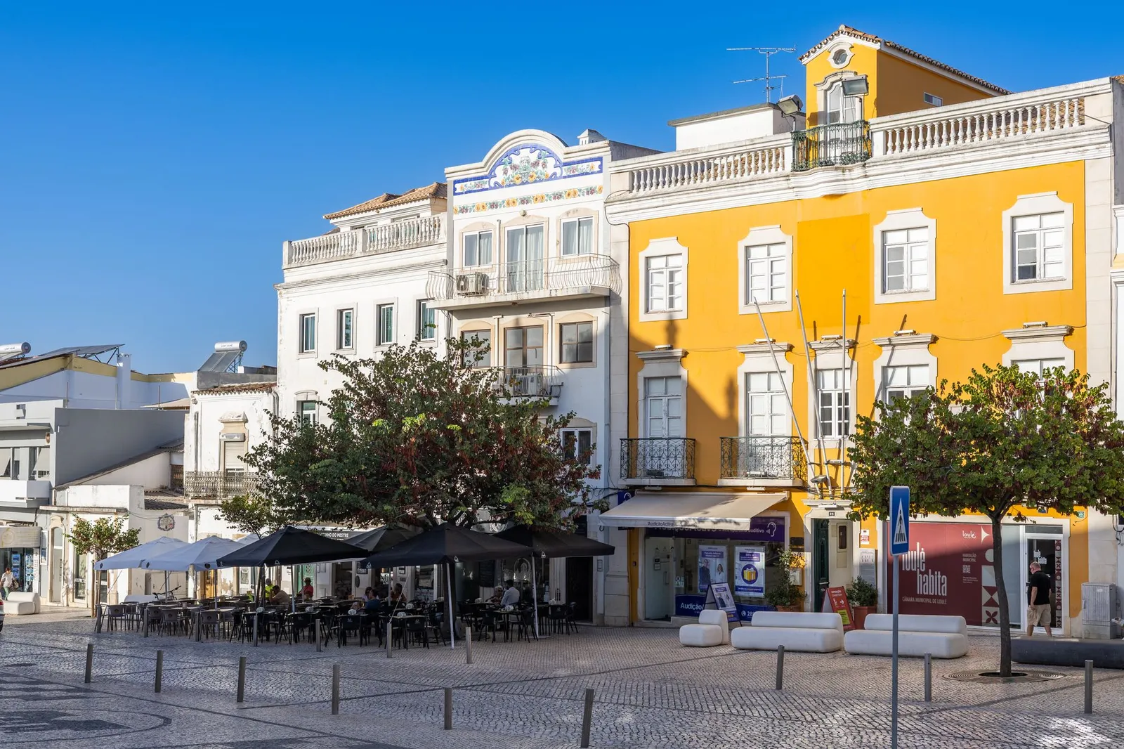 Explore the vibrant architecture and inviting outdoor cafes in a picturesque square in Loulé, Faro, Portugal.