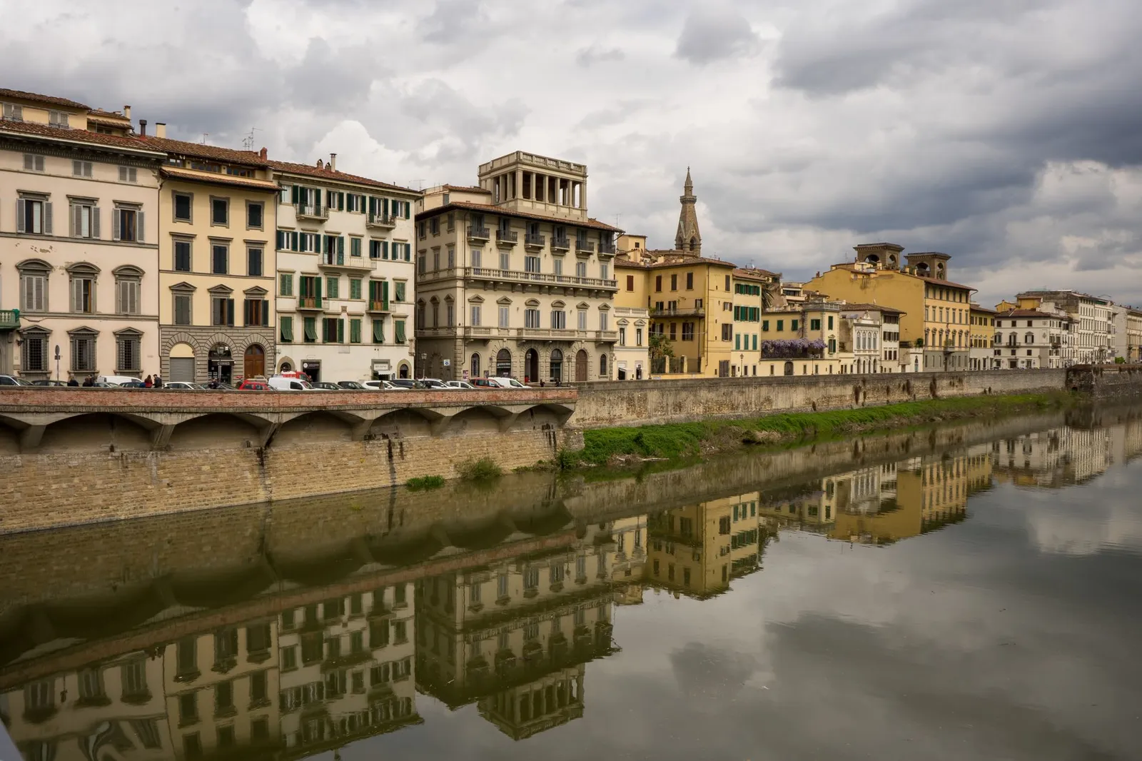 Scenic view of historic buildings reflected in the river in Florence, Italy under cloudy skies.