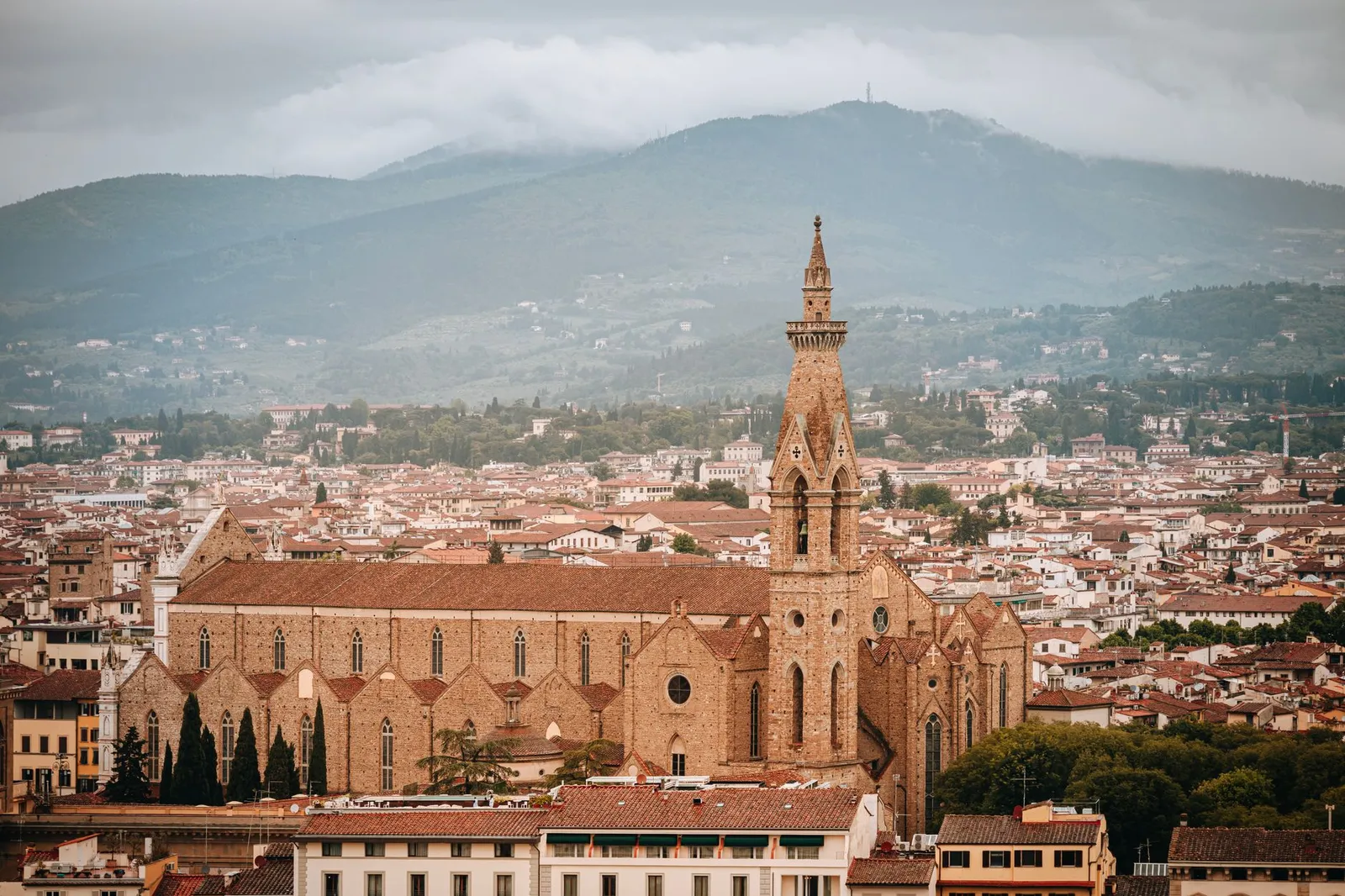 Aerial view of Santa Croce Basilica in Florence, showcasing gothic architecture and vibrant red rooftops.