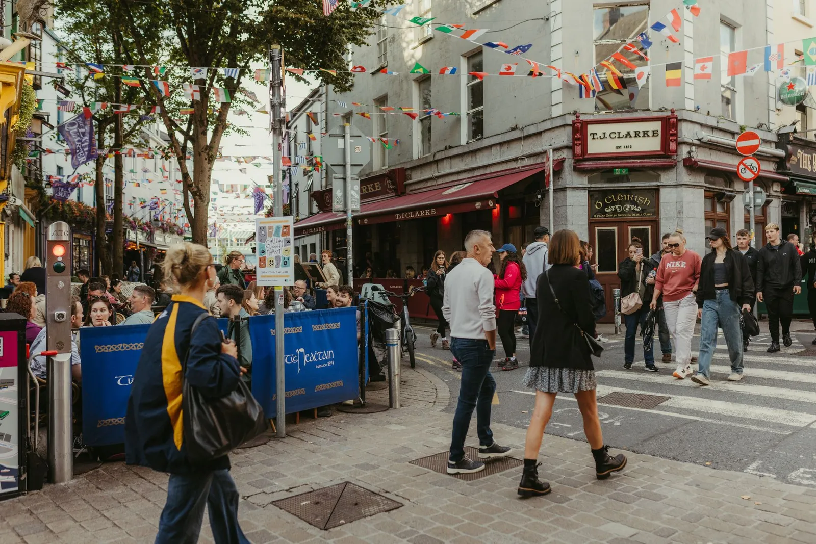 Lively street scene in Galway, Ireland, with people and colorful flags on a vibrant day.