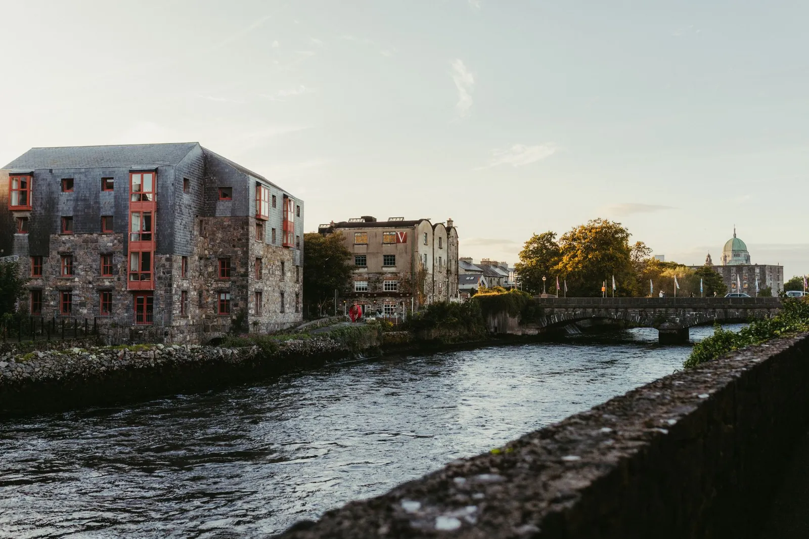 Picturesque view of the river in Galway, Ireland at sunset with historic buildings and a charming bridge.