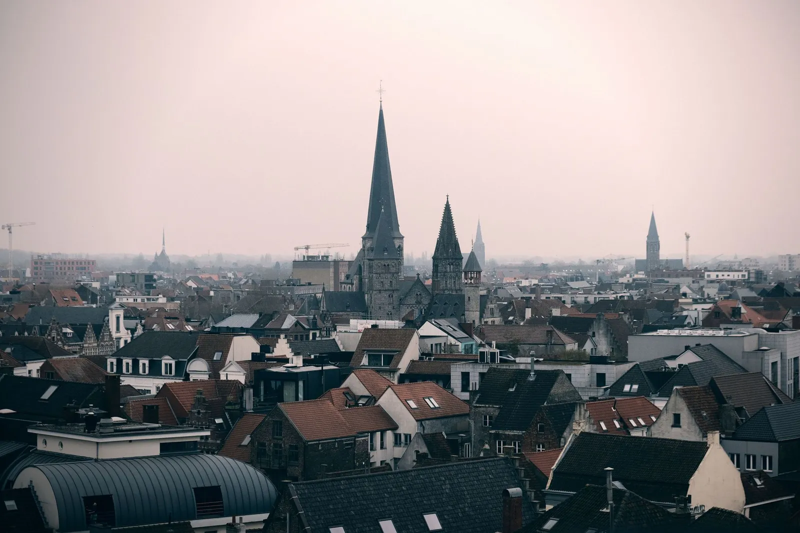Explore Ghent's charming skyline with iconic Gothic architecture, steeples, and historical buildings against a hazy morning sky.