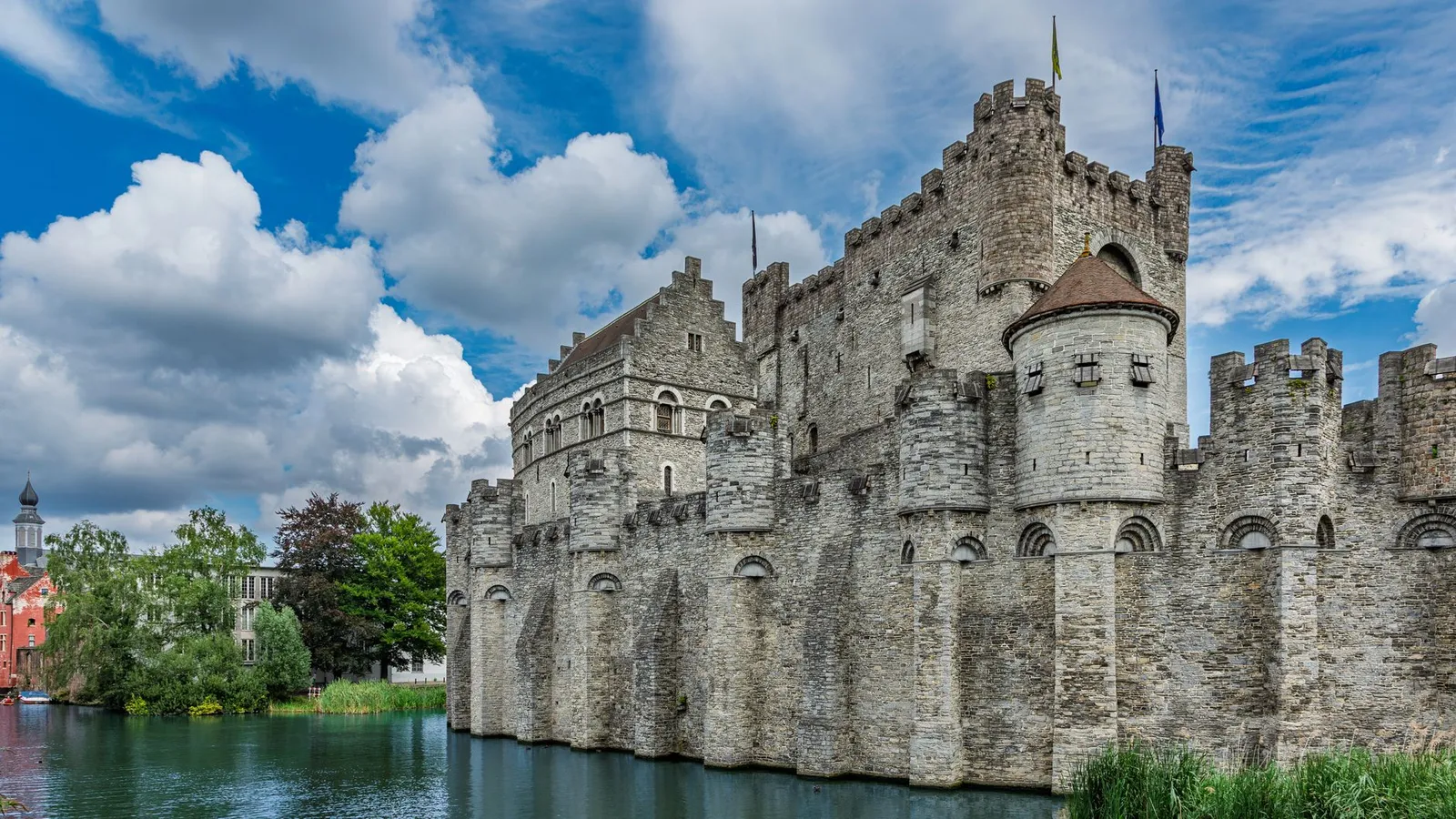 Medieval Gravensteen Castle against a cloudy blue sky in Ghent, Belgium, showcasing stone architecture.