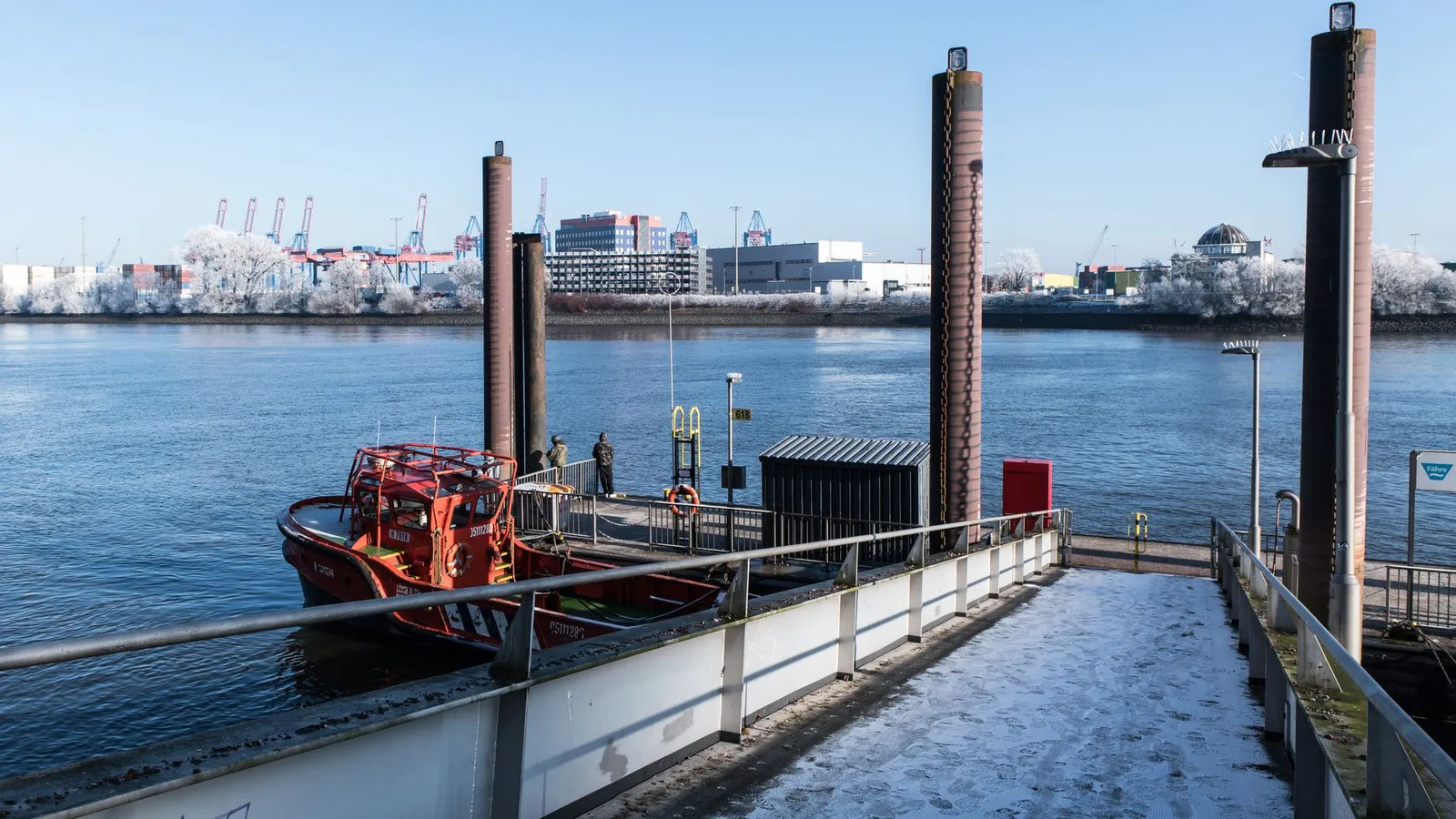 A serene winter view of Hamburg port with a frost-covered jetty and a moored boat.