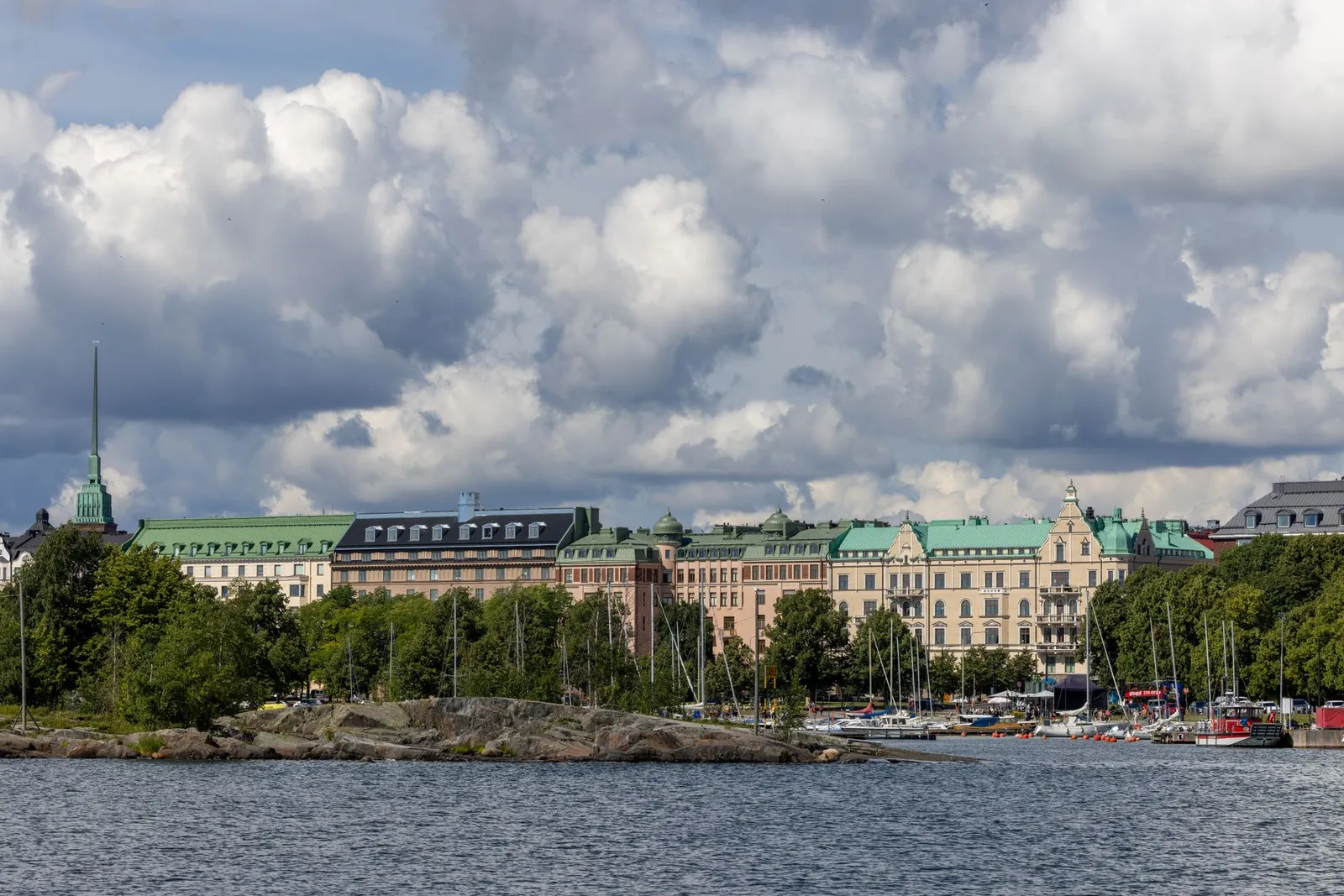Urban landscape of Helsinki with historic buildings along the waterfront under a cloudy sky.