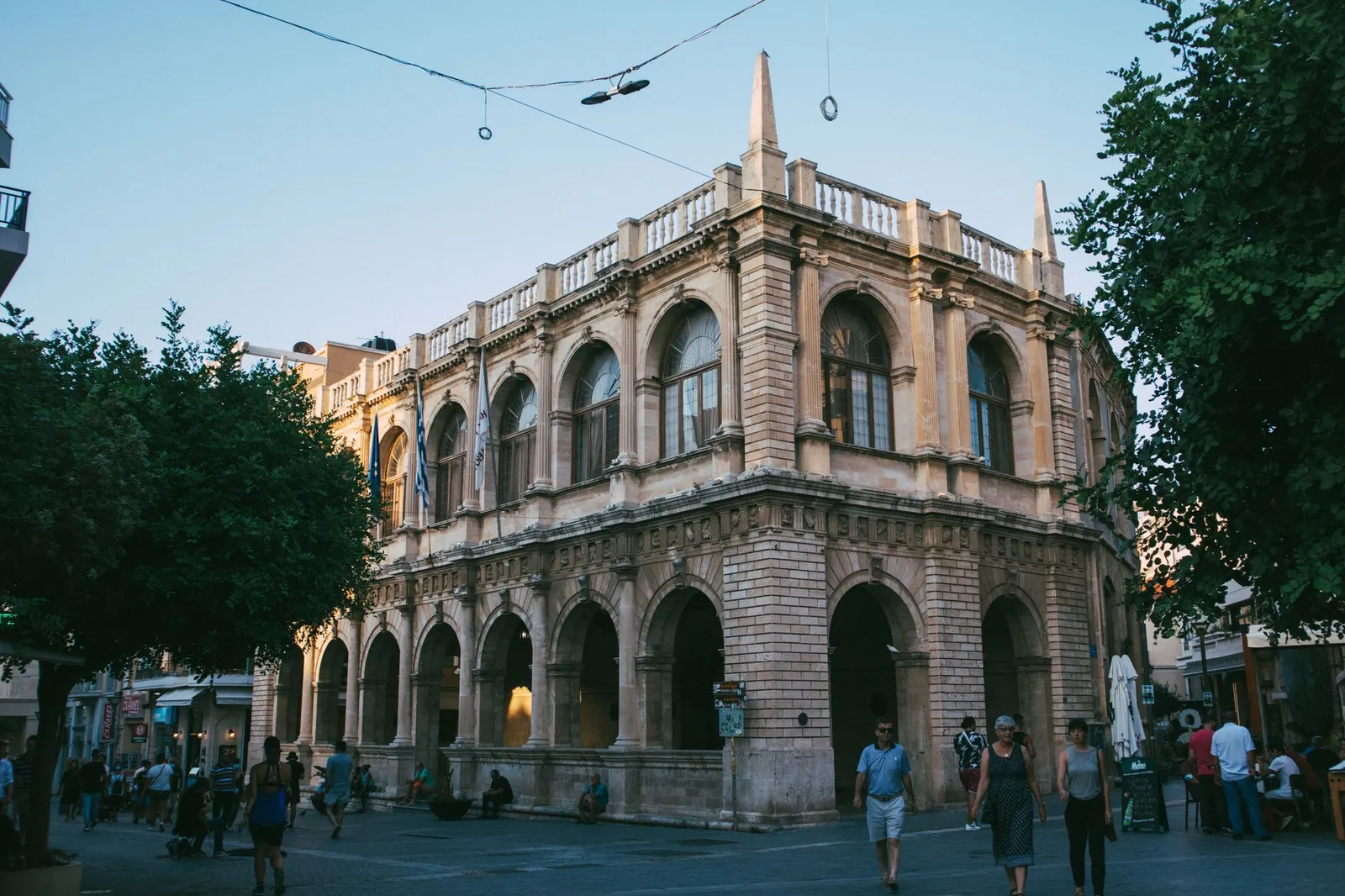 A picturesque historic building in a European town square captured at dusk, with people strolling nearby.