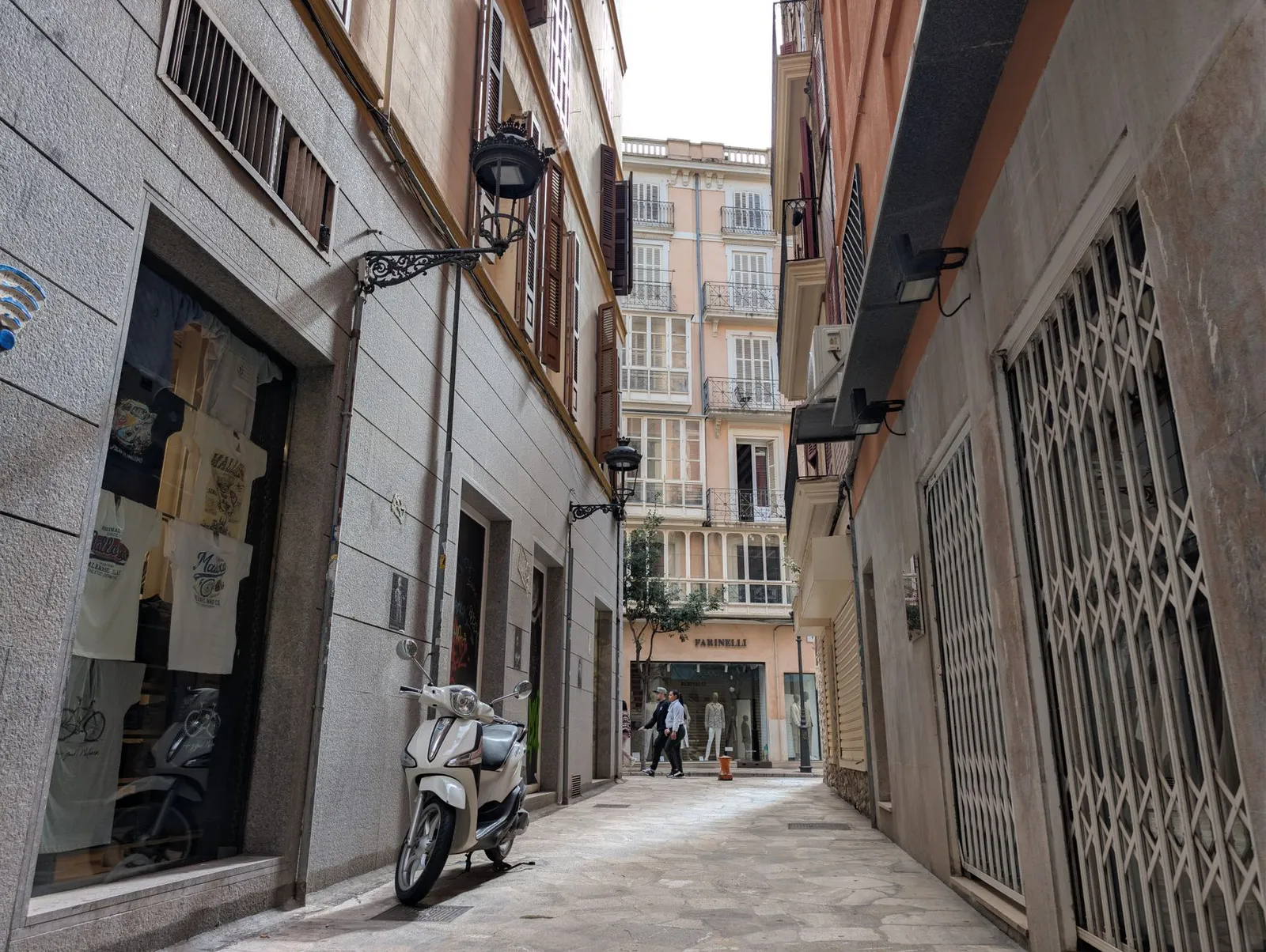 Picturesque alleyway in Ibiza with scooter and people, showcasing traditional Spanish architecture.