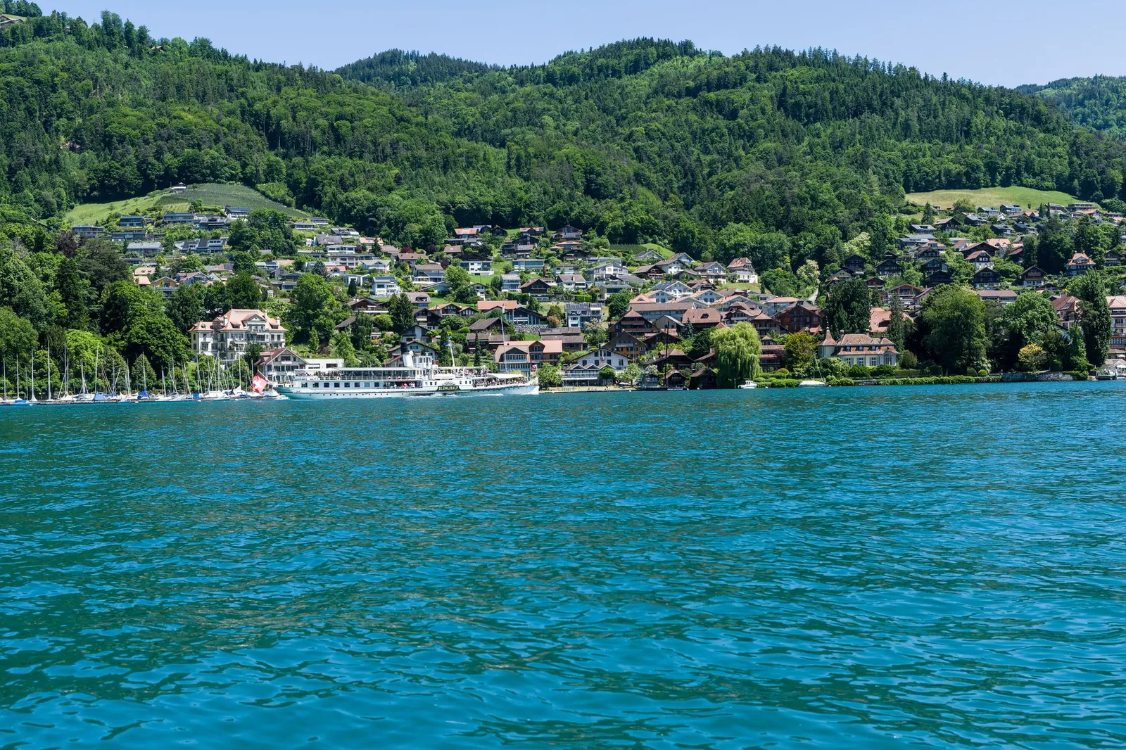 Picturesque lakeside view of a Swiss village nestled by Lake Brienz with lush green hills.