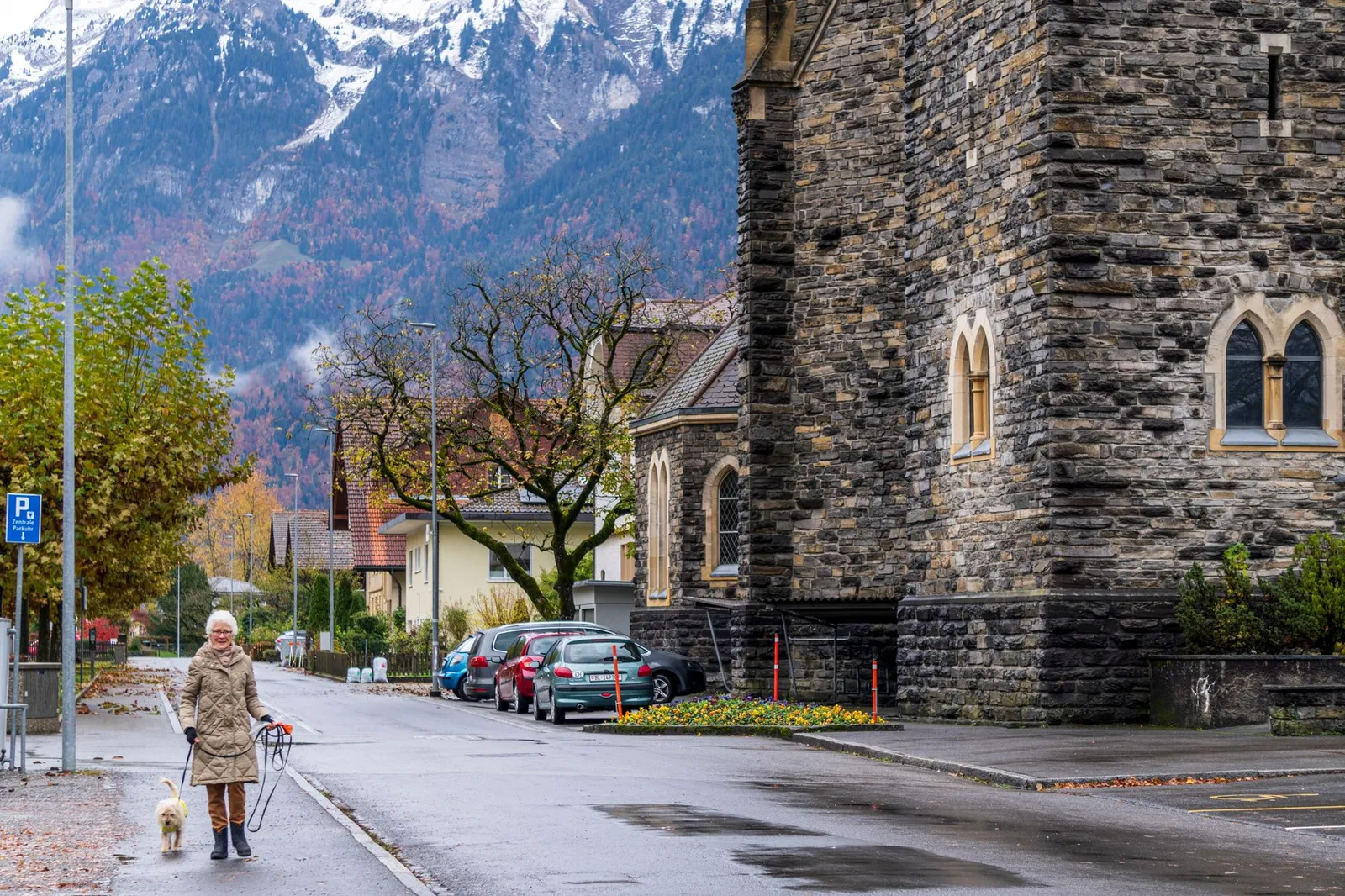 A woman walks her dog near a stone church in Interlaken with autumn scenery.