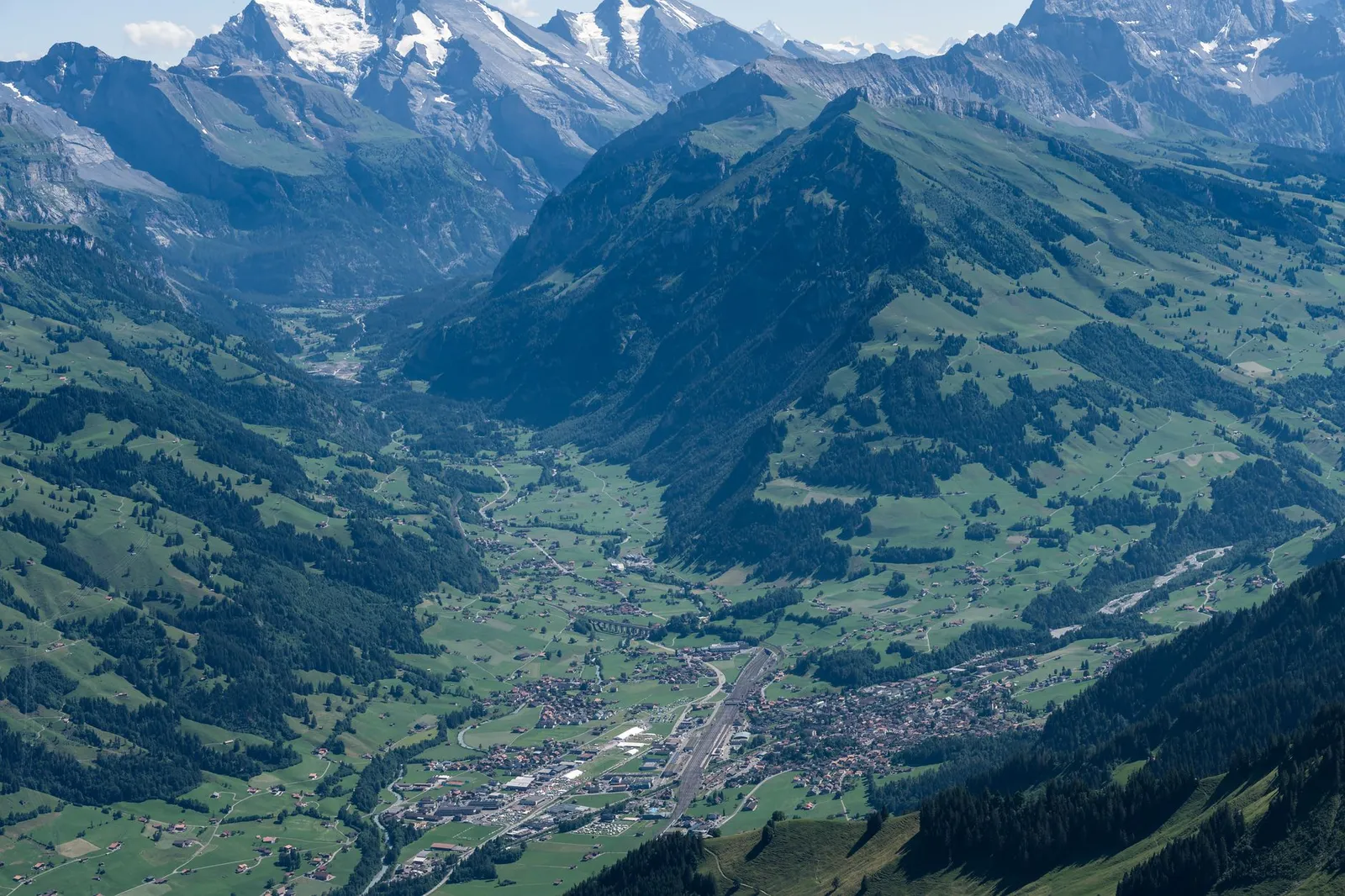A breathtaking aerial view of the Swiss Alps highlighting lush valleys and towering peaks under a clear summer sky.
