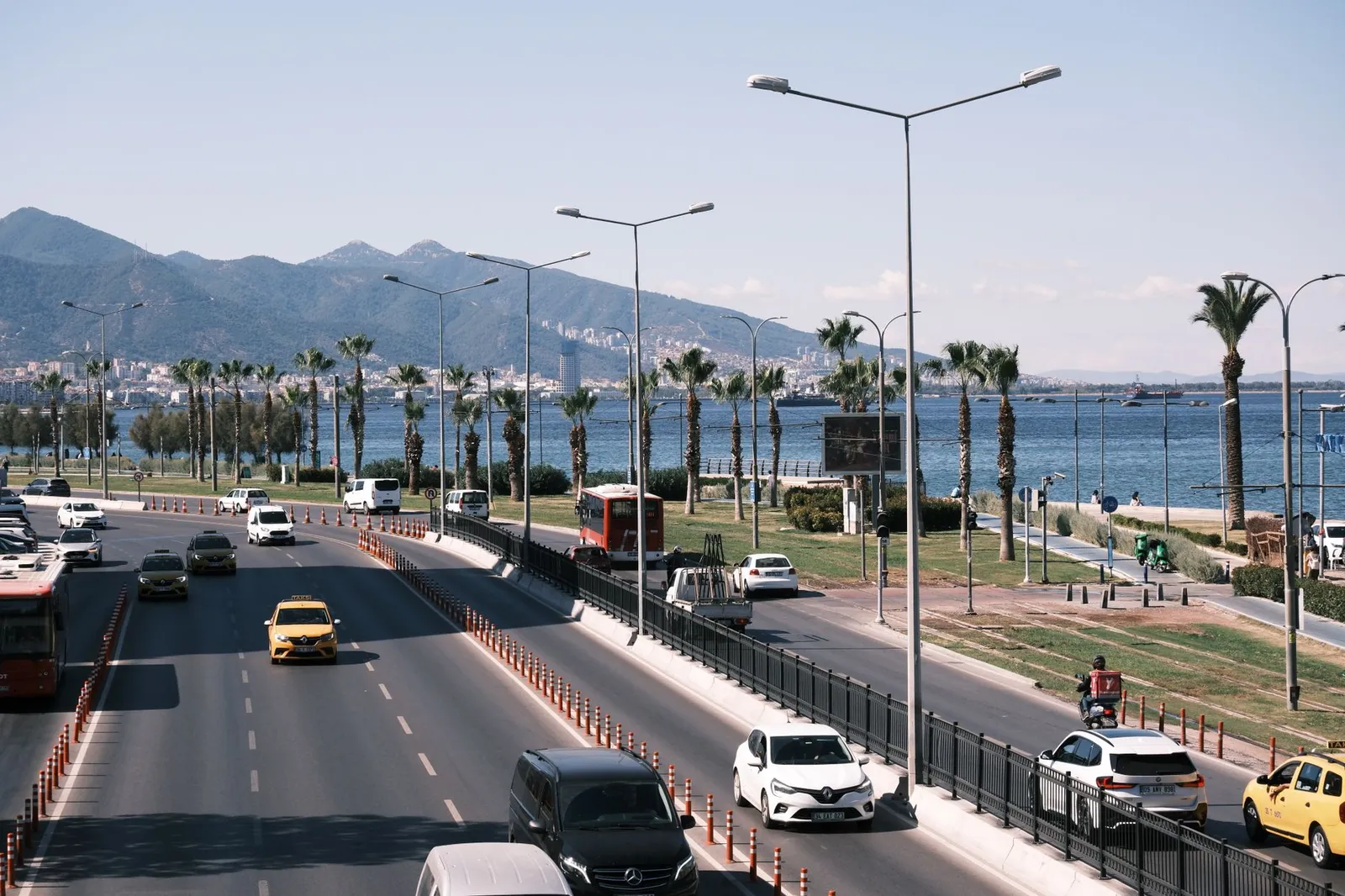 Daytime city traffic along the scenic seafront highway in Izmir, Turkey, with mountain views.