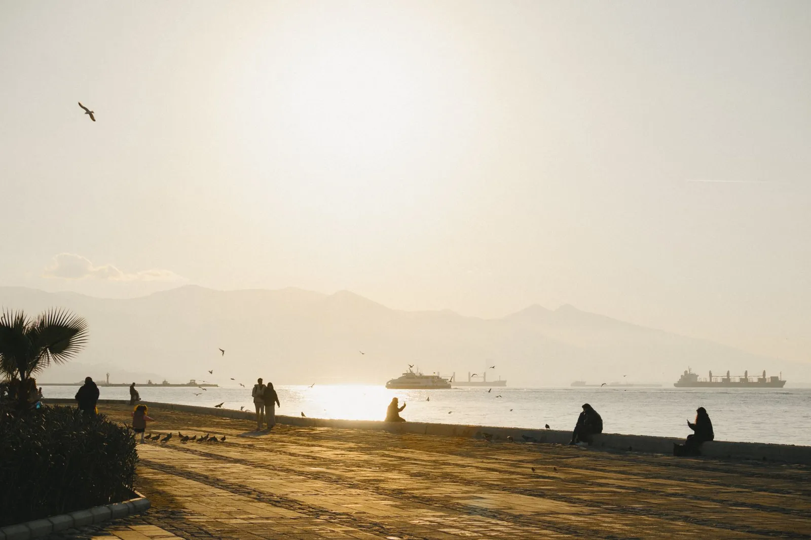 Serene sunset view over Izmir promenade with ships and people silhouetted against the sea.