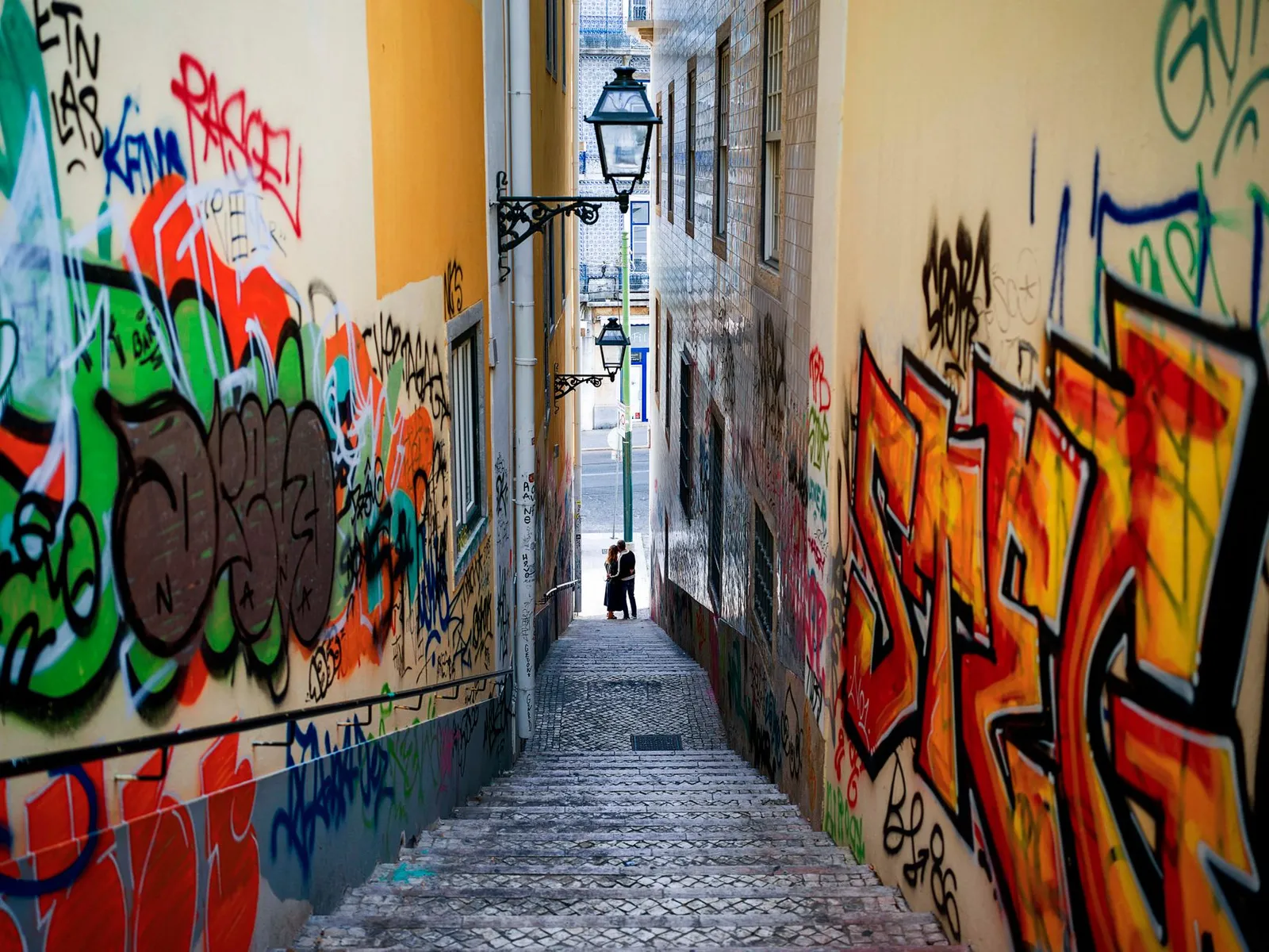 Vibrant graffiti decorates a narrow alley in Lisbon, Portugal, offering a glimpse of urban art.