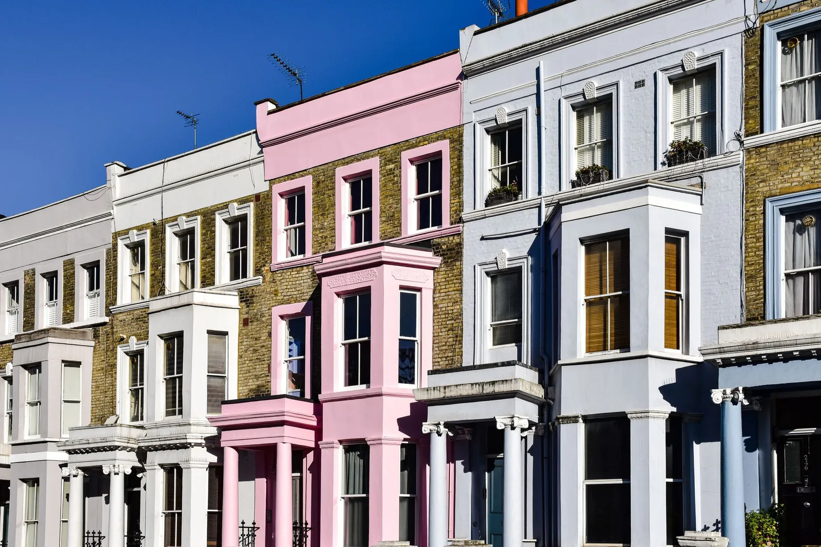 Vibrant multi-colored Victorian row houses in Notting Hill, bathed in sunlight under a clear blue sky.