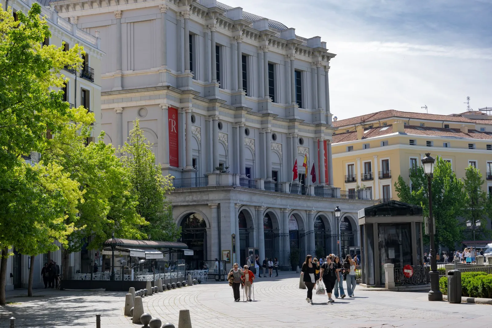 Daytime view of the Teatro Real in Madrid, with people strolling by, under clear skies.