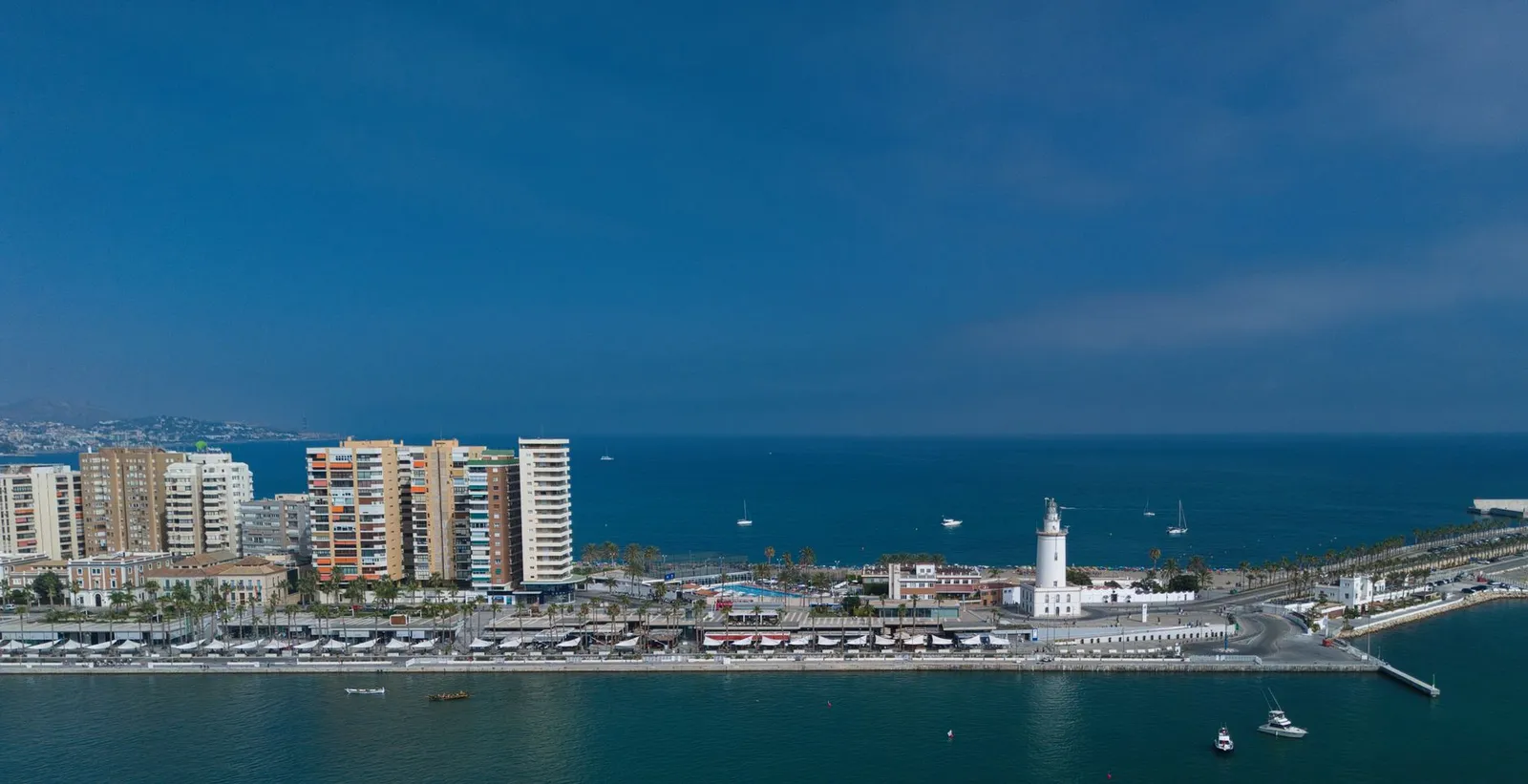 A captivating aerial shot of Málaga harbor showcasing the waterfront, skyline, and iconic lighthouse under a clear blue sky.