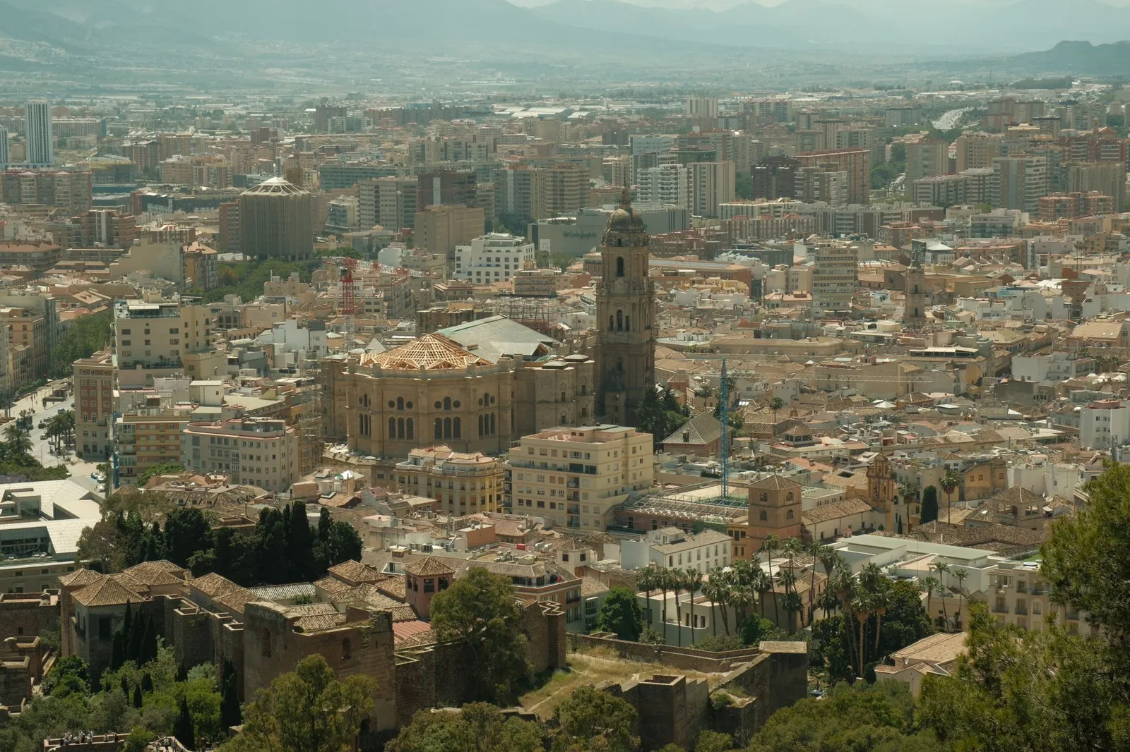Aerial view capturing the bustling cityscape of Málaga, featuring the iconic Cathedral of Málaga amid urban and natural surroundings.