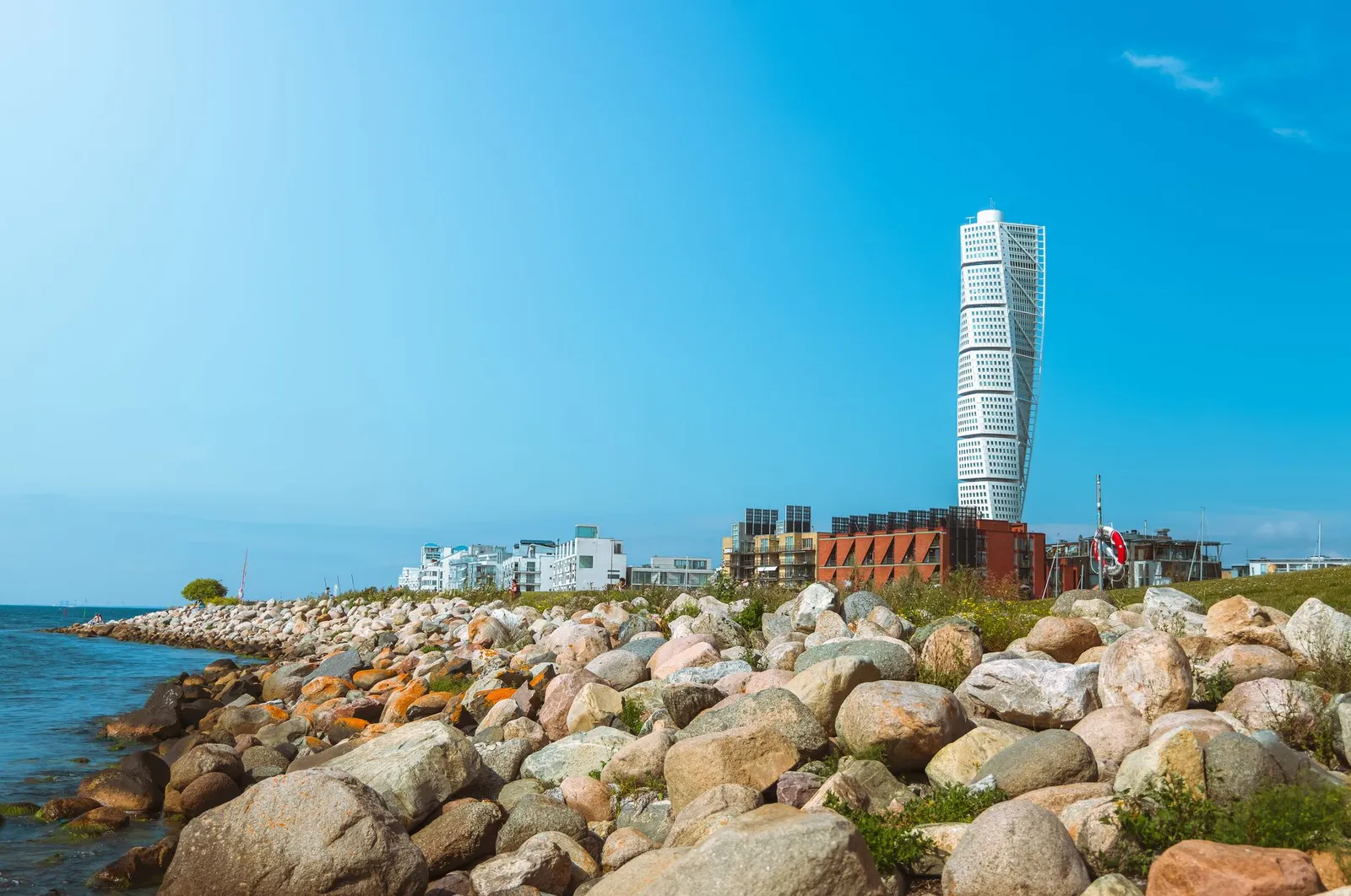 Iconic Turning Torso tower beside a rocky coastline in Malmö, with a clear blue sky.