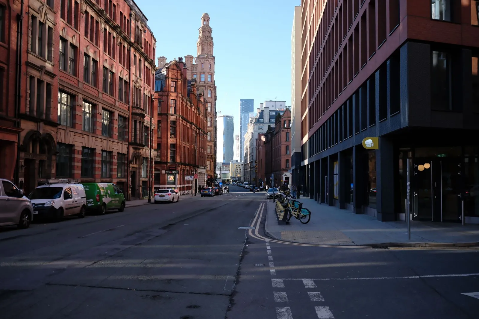 Urban streetscape in Manchester, showcasing modern and historic architecture under a clear blue sky.