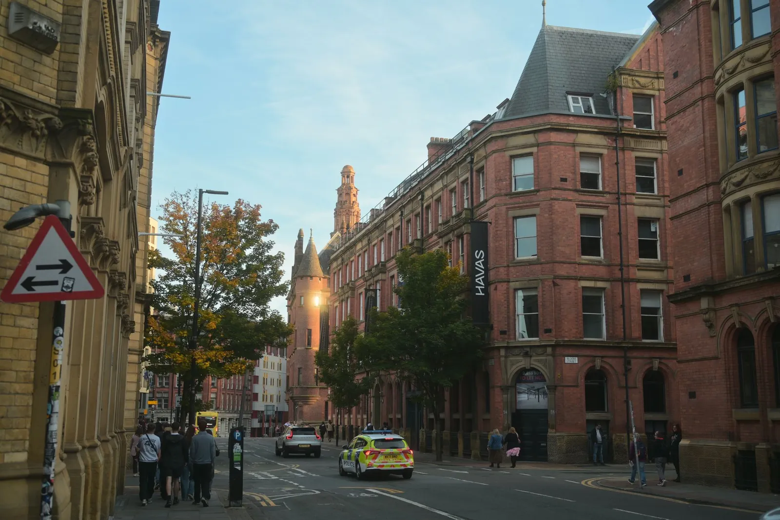 Evening view of a busy street in Manchester with historic brick architecture and people walking.