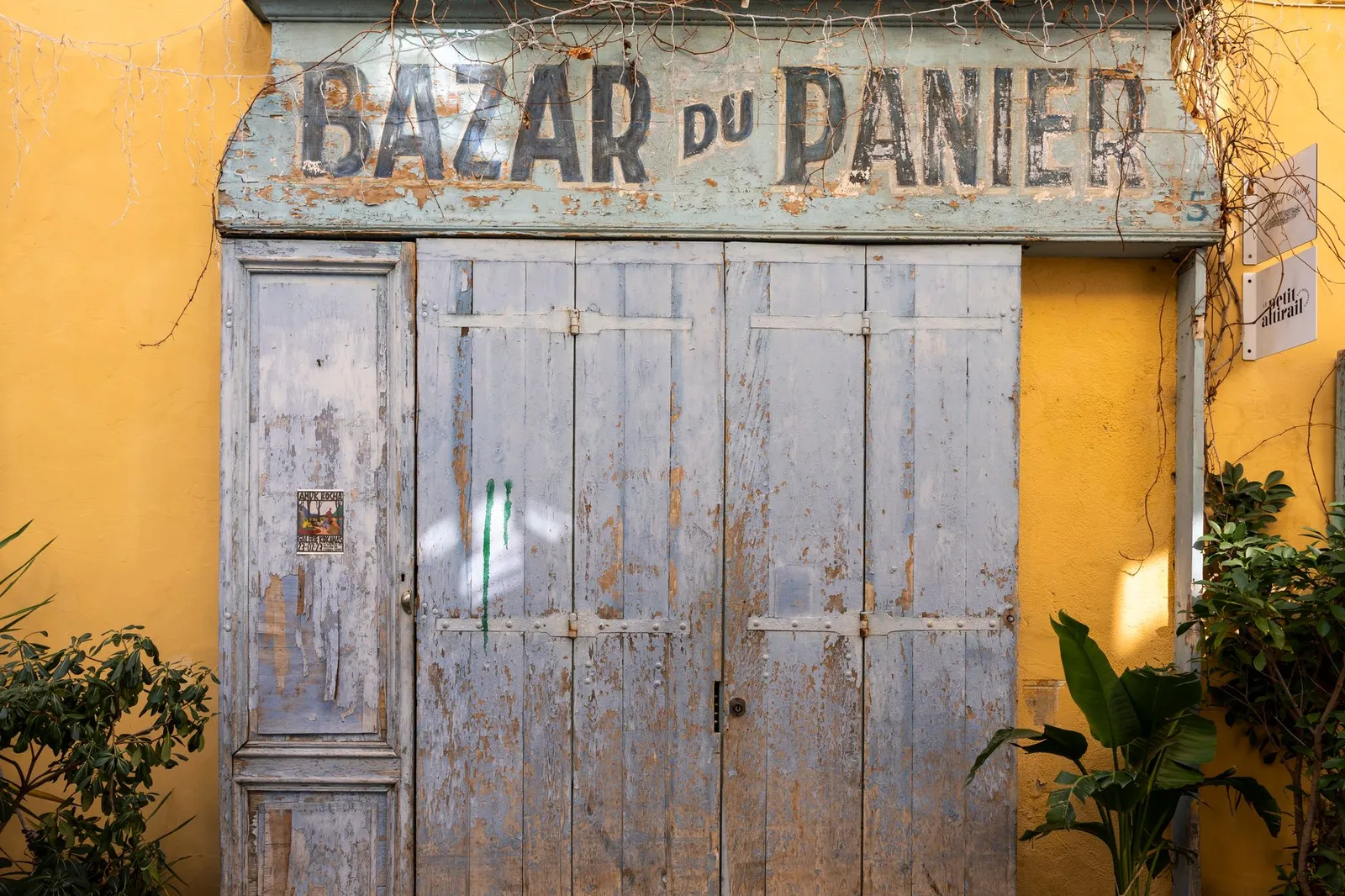Rustic wooden door of the historic Bazar du Panier in a sunny French street.
